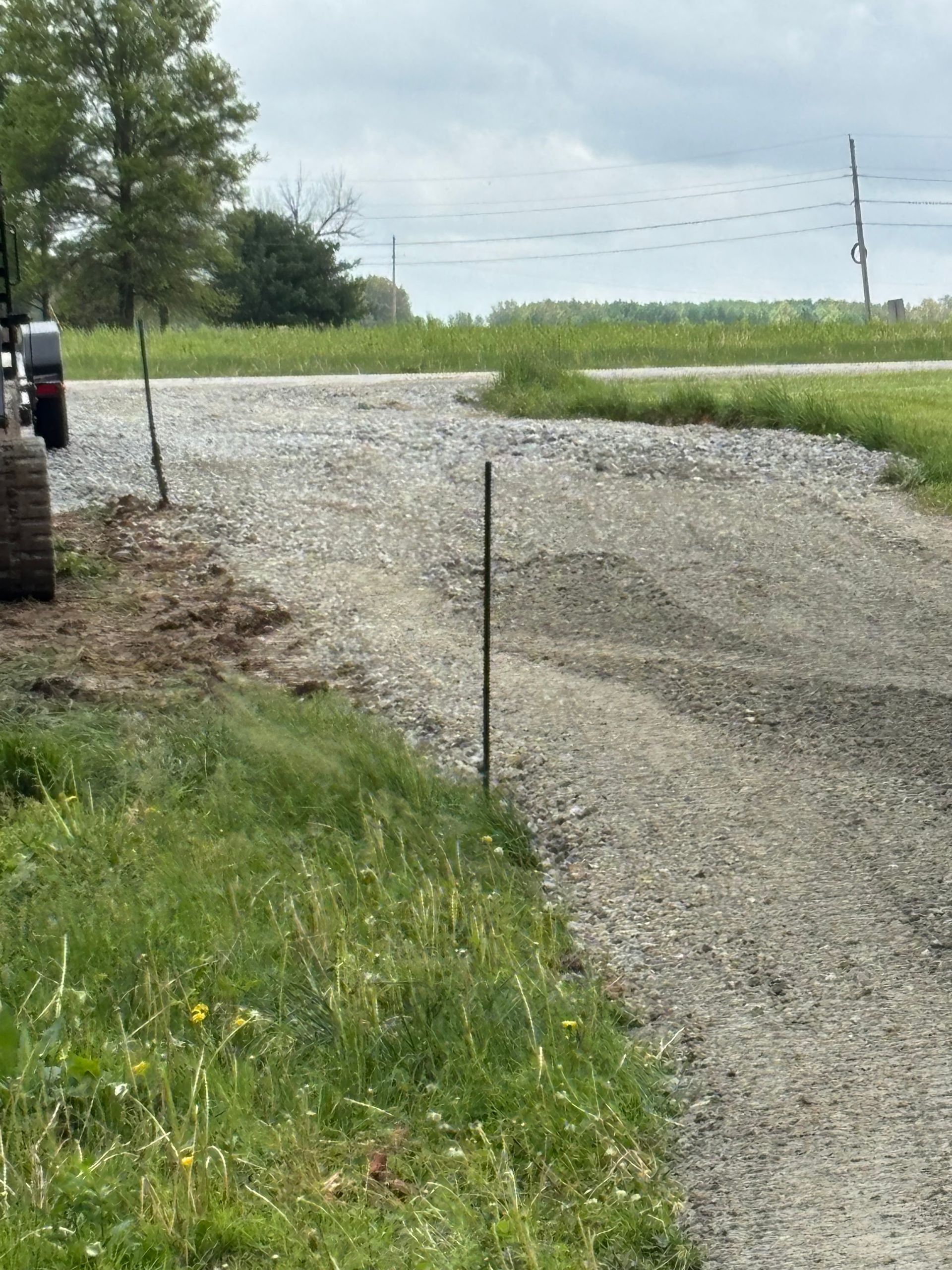 Gravel driveway under construction beside a grassy field on an overcast day