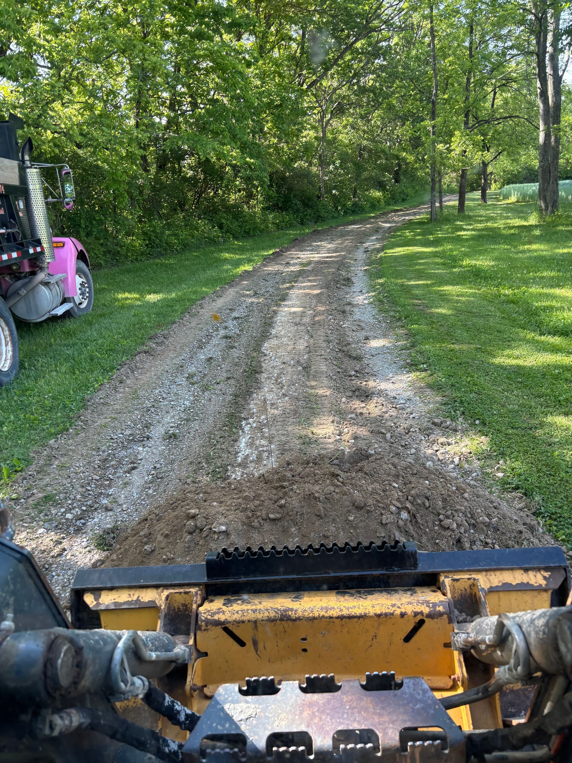 View from a skid steer driving up a muddy gravel path through a wooded yard