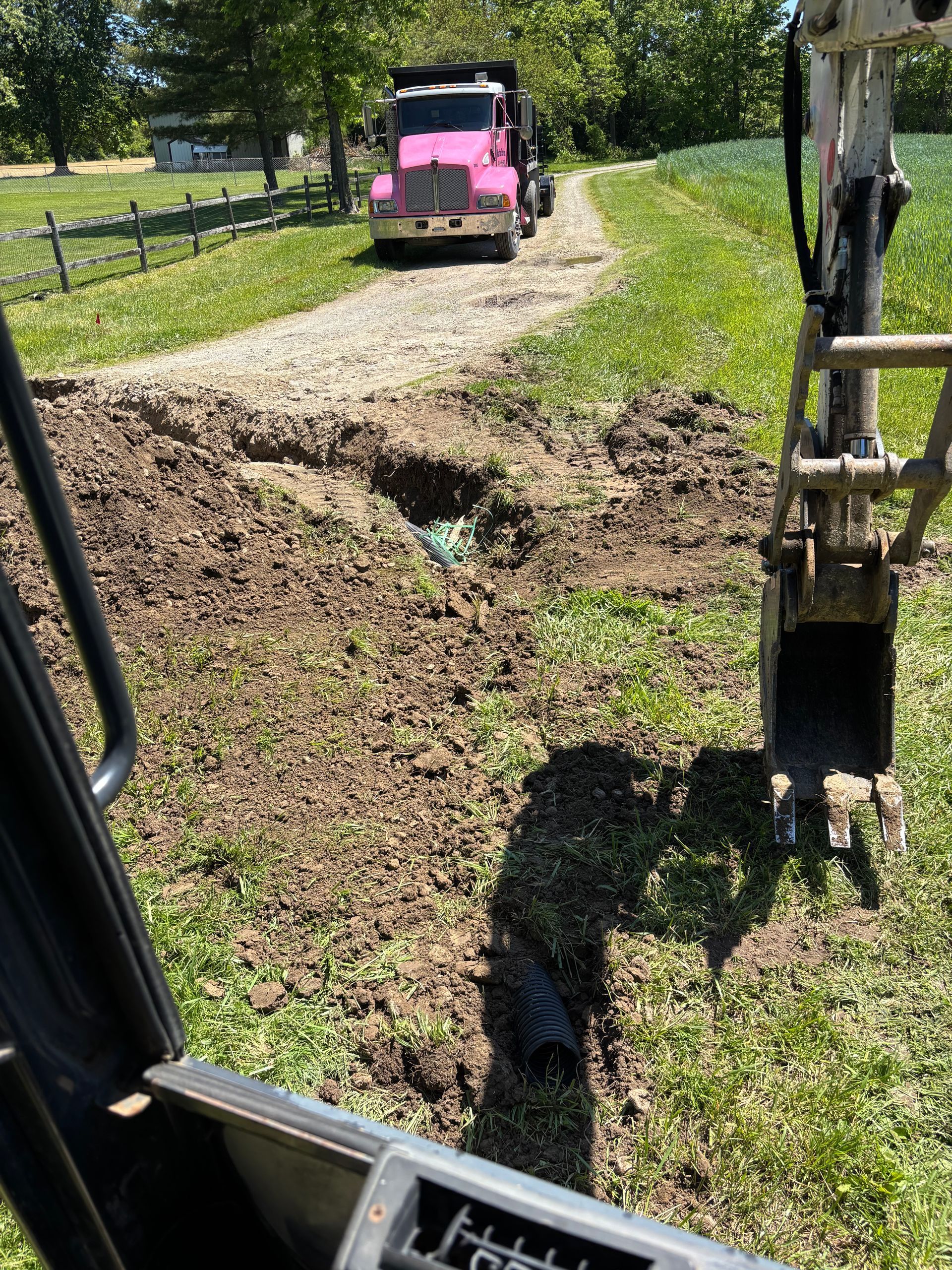 Pink jeep near a muddy washout on a rural dirt road, seen from inside a construction vehicle