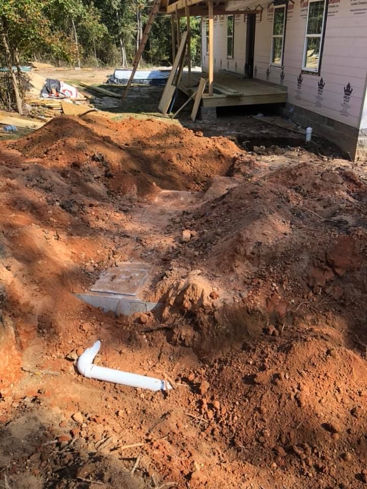 Construction site with dirt piles and exposed plumbing near a partially built house with a porch.