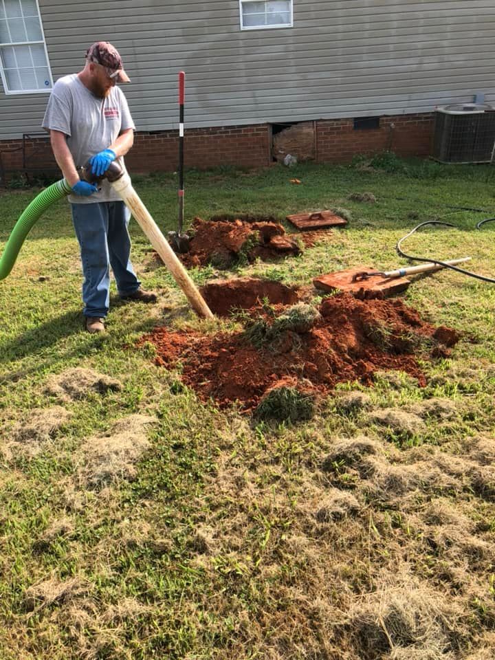 Man operating a septic tank pump in a yard, removing dirt from a hole.
