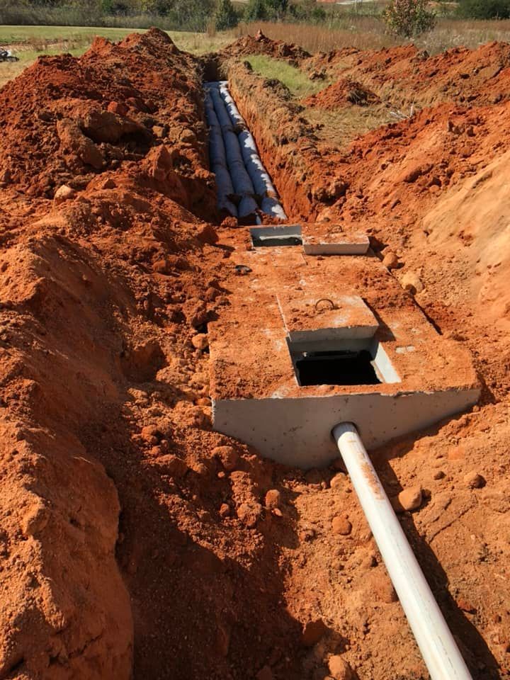 Trench in red soil with gray pipes, and a concrete access box.