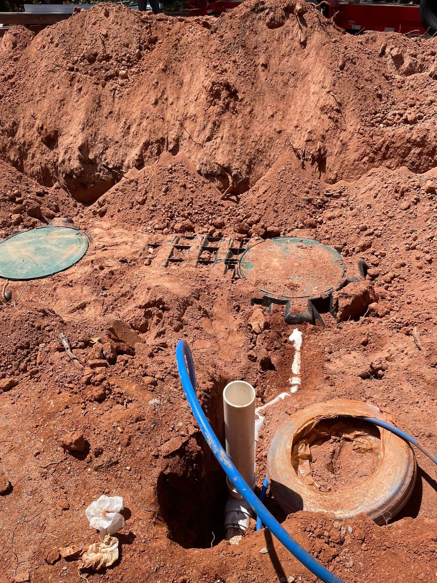 Excavated septic system components in red dirt, including lids, pipes, and a blue hose.