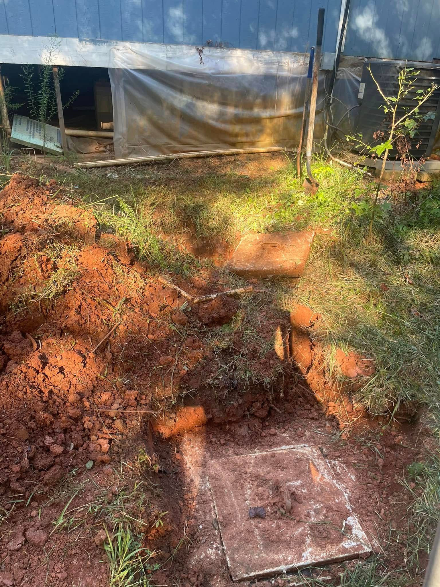 Excavated ground with a square metal access cover in front of a building.