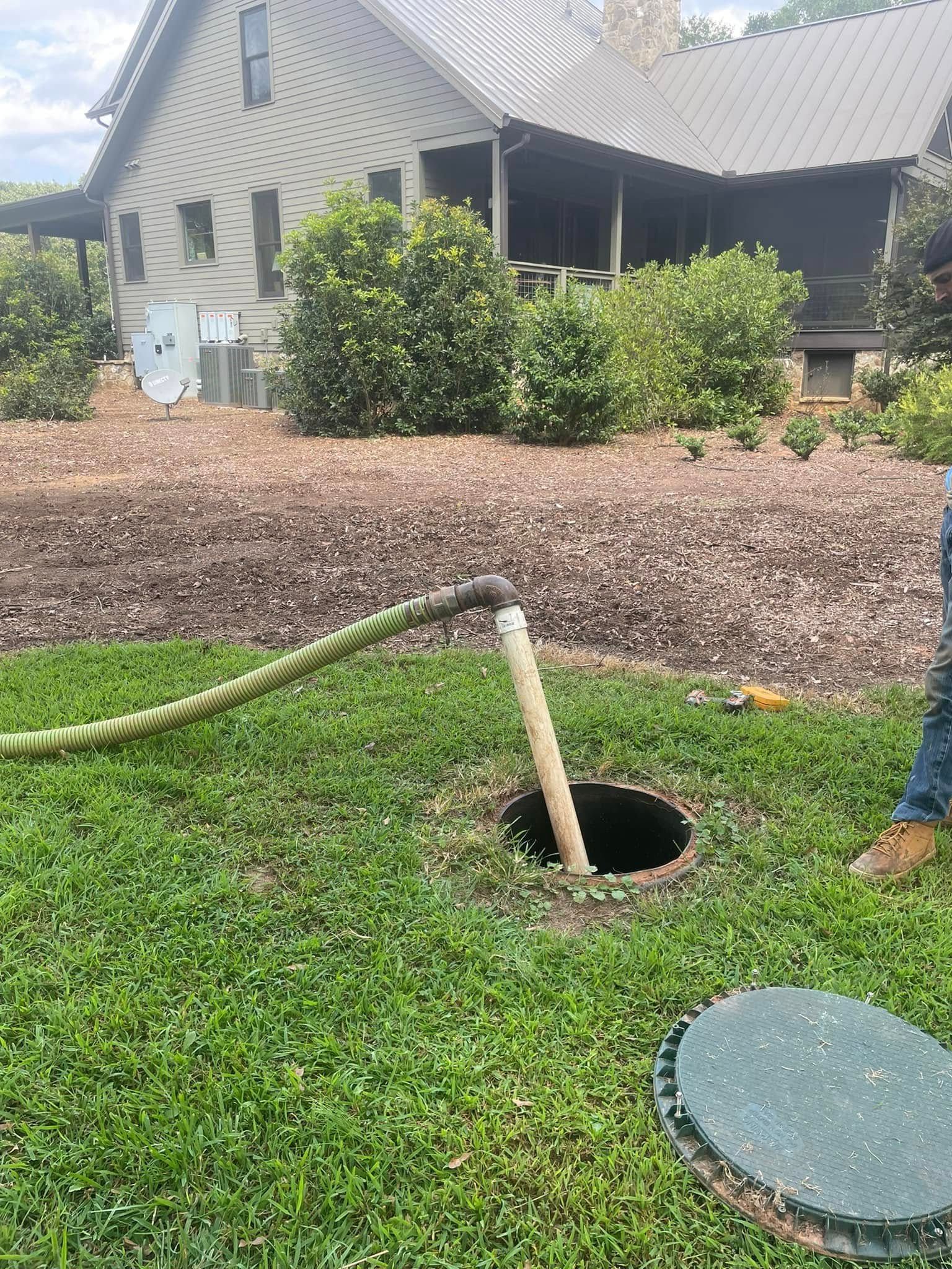 Septic tank being serviced in a grassy yard, with a hose extending from the open tank to a truck.
