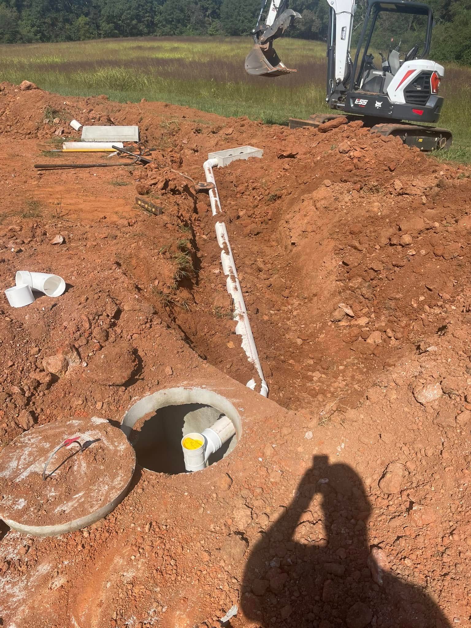 Excavated septic tank and plumbing. A small excavator and red clay soil.
