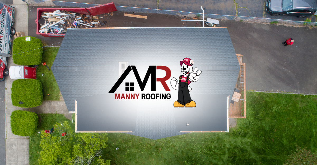 Aerial view of a gray roof with AMR Manny Roofing logo, beside a green lawn and driveway.