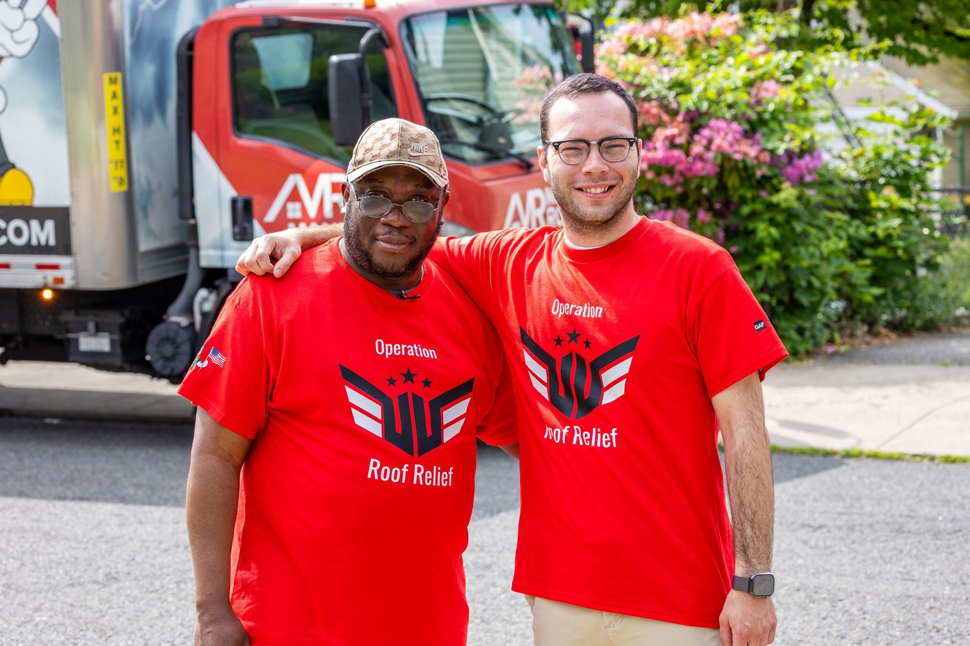 Two men in red shirts are posing for a picture in front of a truck.