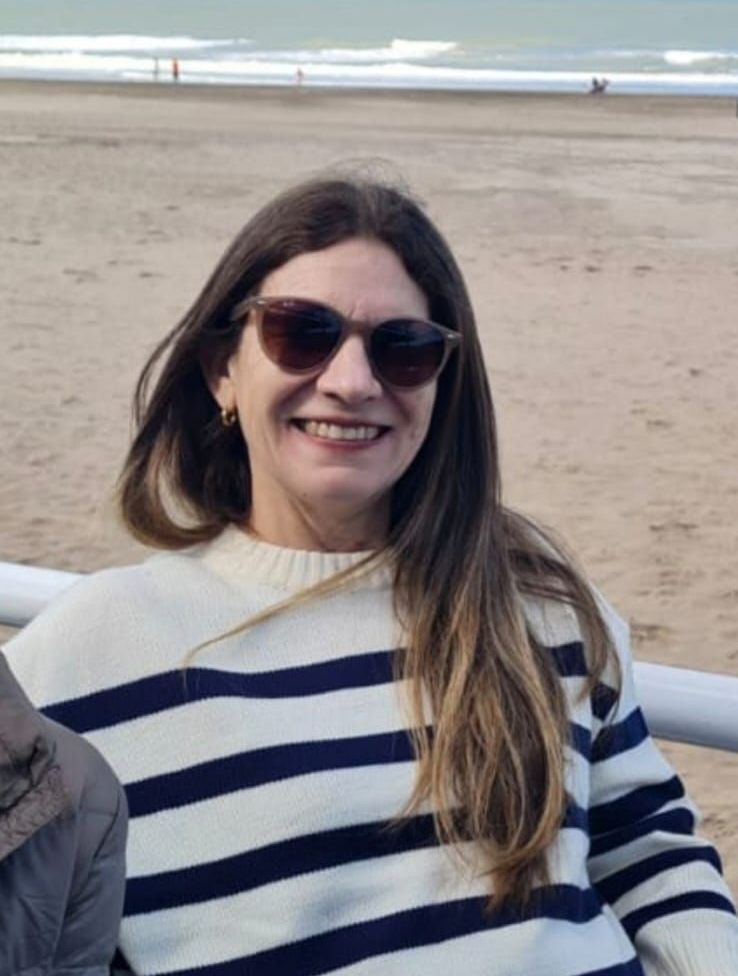 Una mujer con gafas de sol y un suéter de rayas sonríe en la playa.