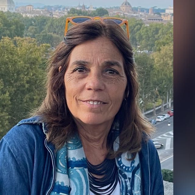 Una mujer con gafas de sol y bufanda sonríe a la cámara.