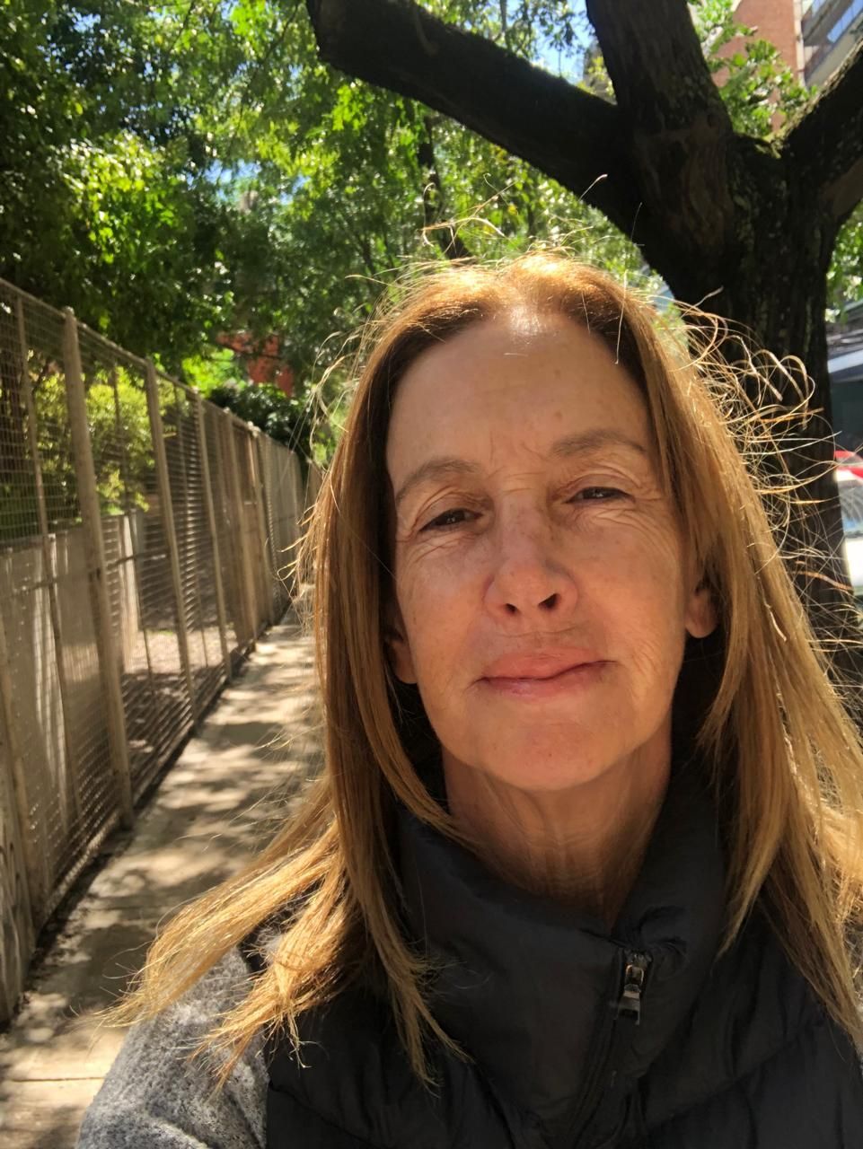 Una mujer se está tomando un selfie en una acera al lado de un árbol.