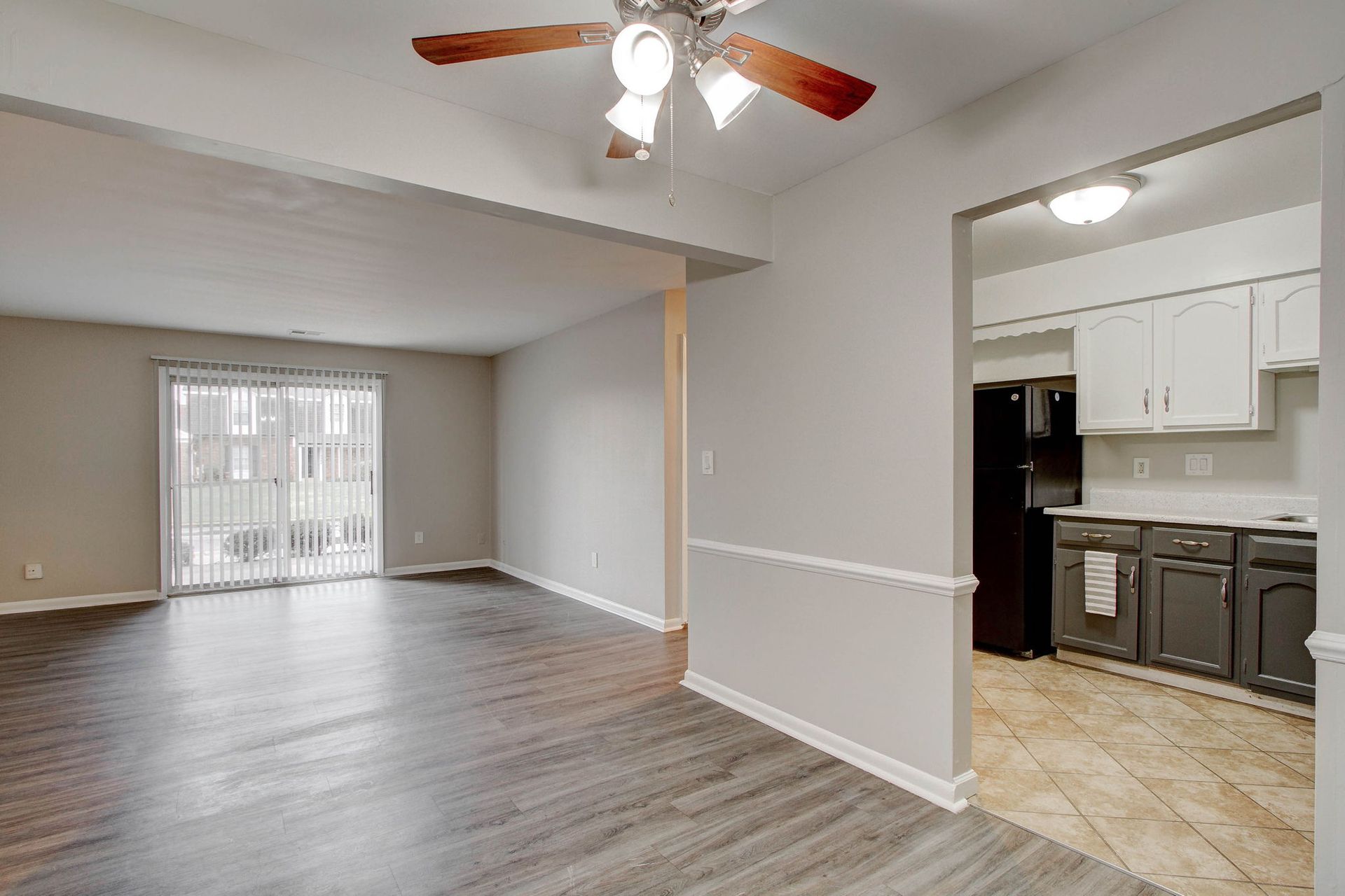 Living room with gray walls, wood floor, and sliding glass door. Kitchen visible.
