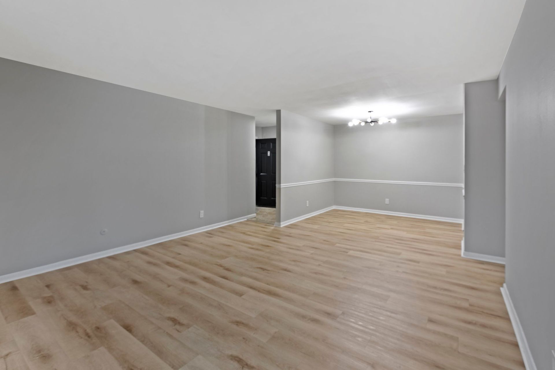 Empty living space with grey walls, wood floors, and a light fixture.