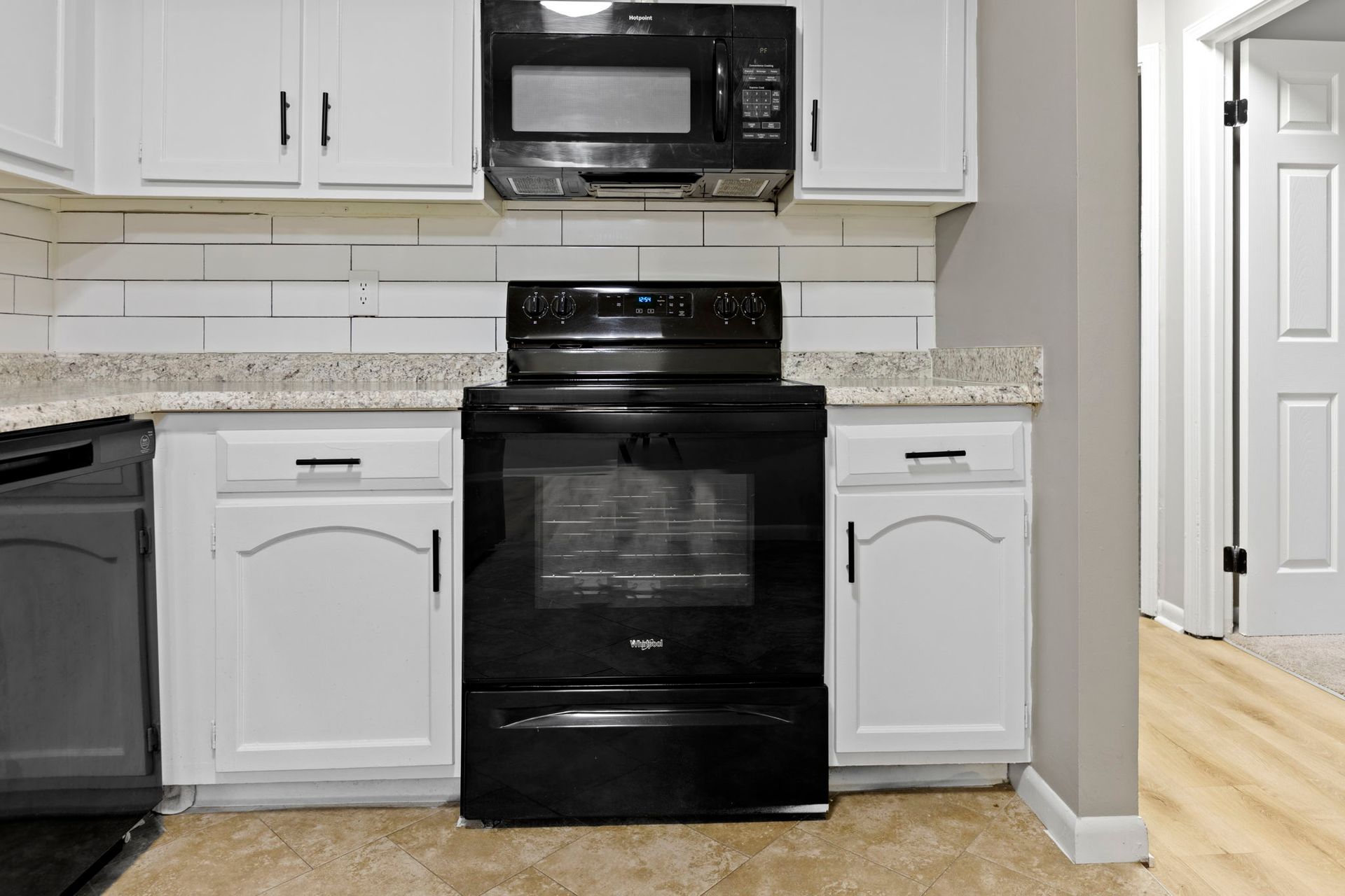 Kitchen with white cabinets, black appliances, light countertops and a door in the background.