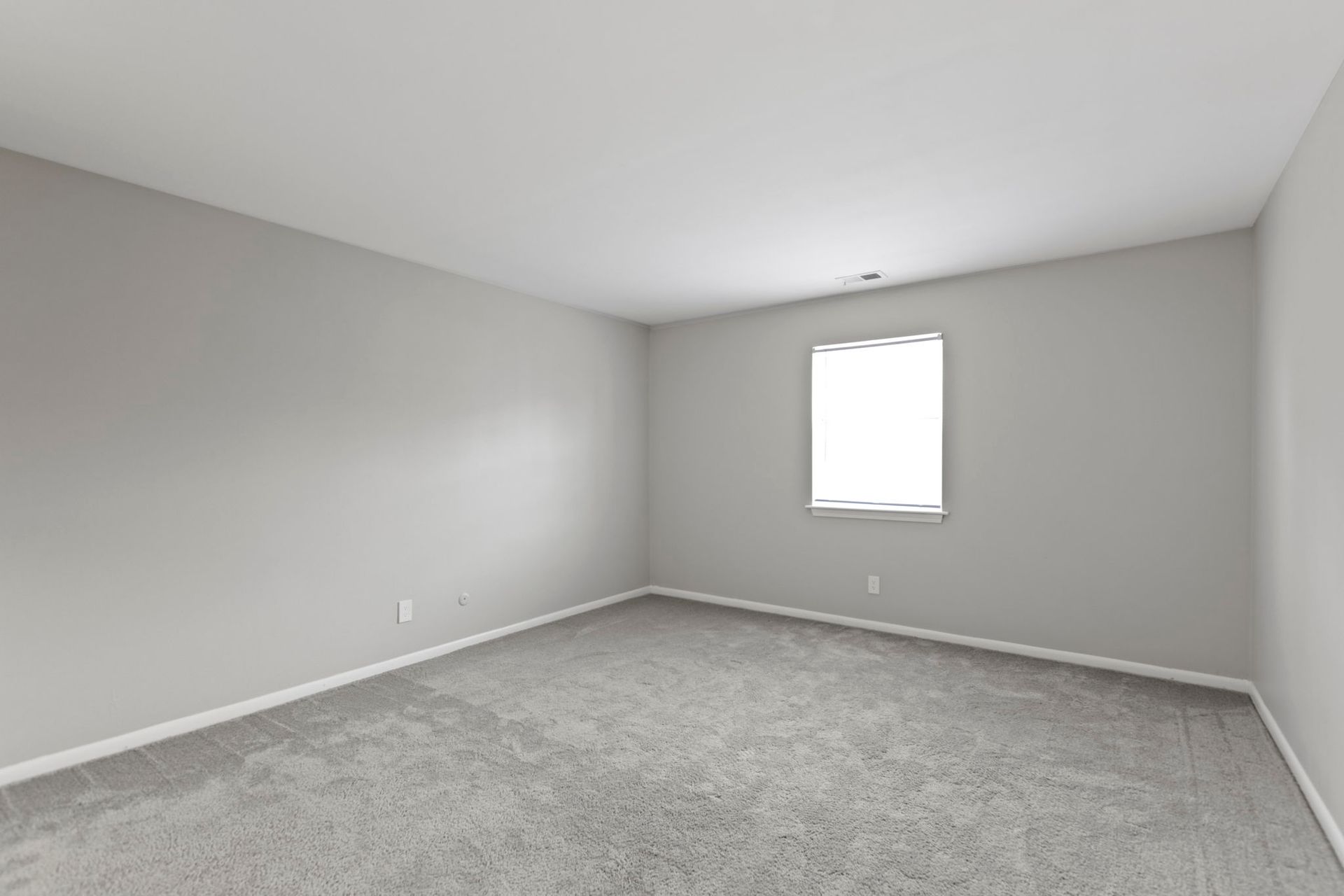 Empty room with gray walls and carpet, a window, and white ceiling.