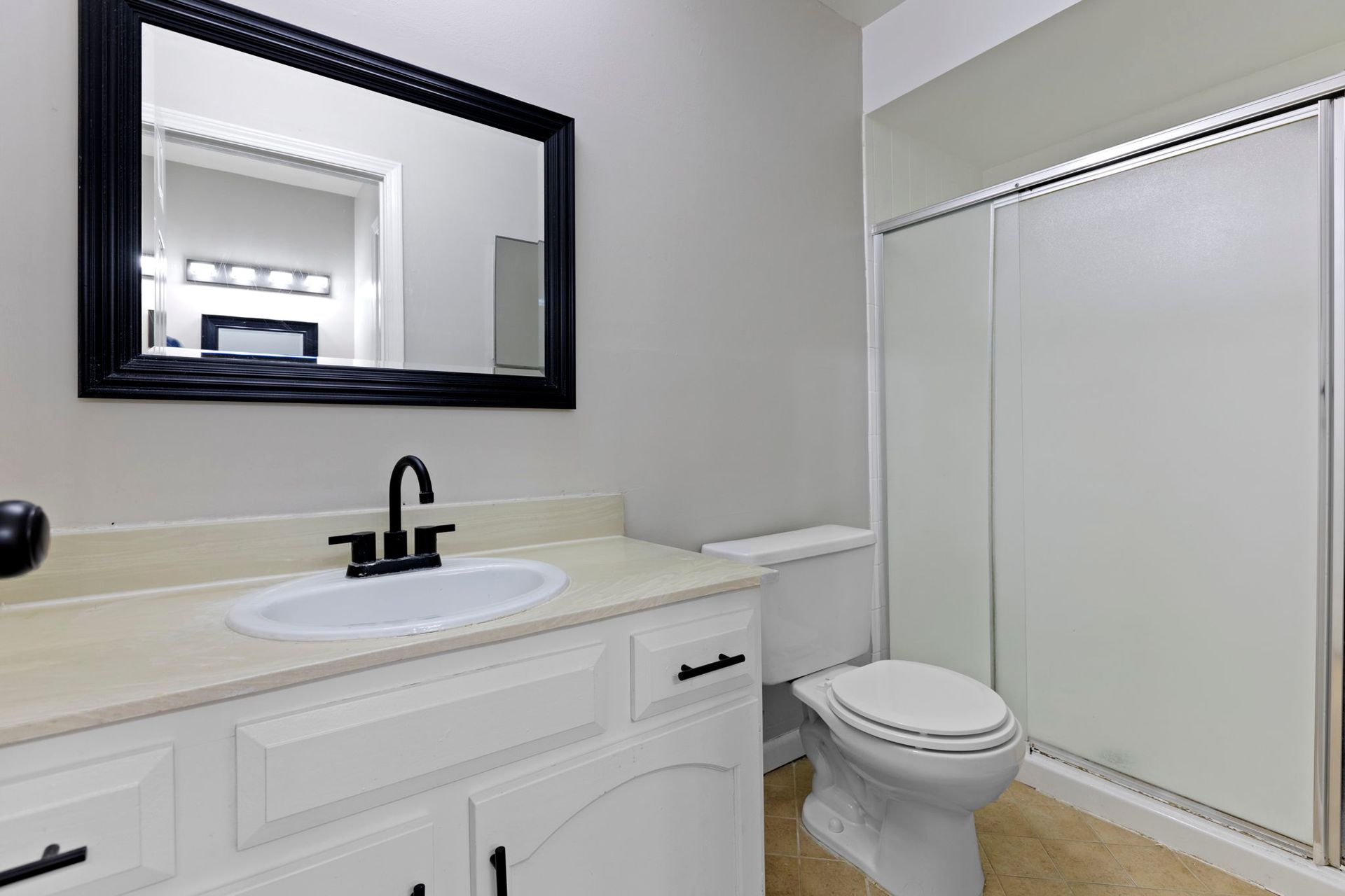Bathroom with white vanity, black fixtures, and a framed mirror. A toilet and shower are visible.