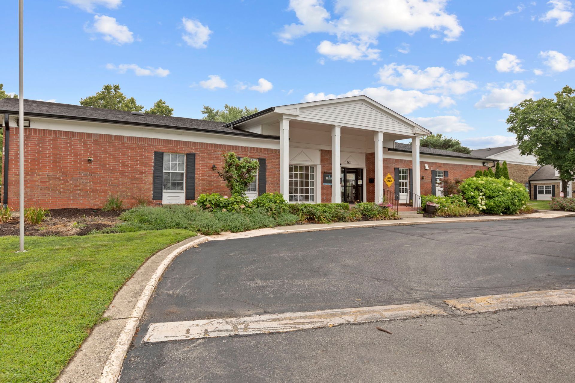 Red brick building with white columns, surrounded by green grass and a black asphalt road.