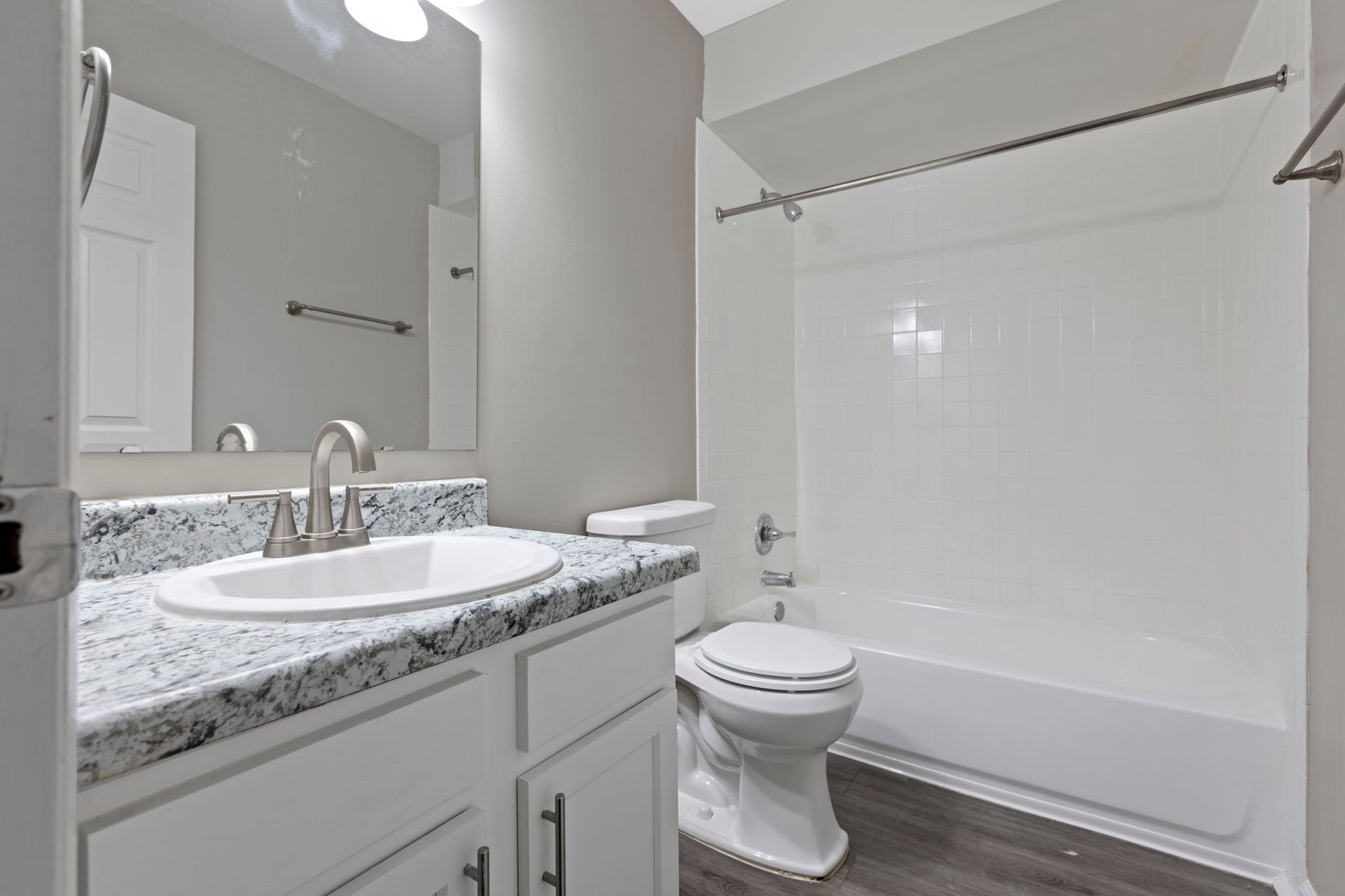 Bathroom with white vanity, sink, toilet, tub, and gray walls.