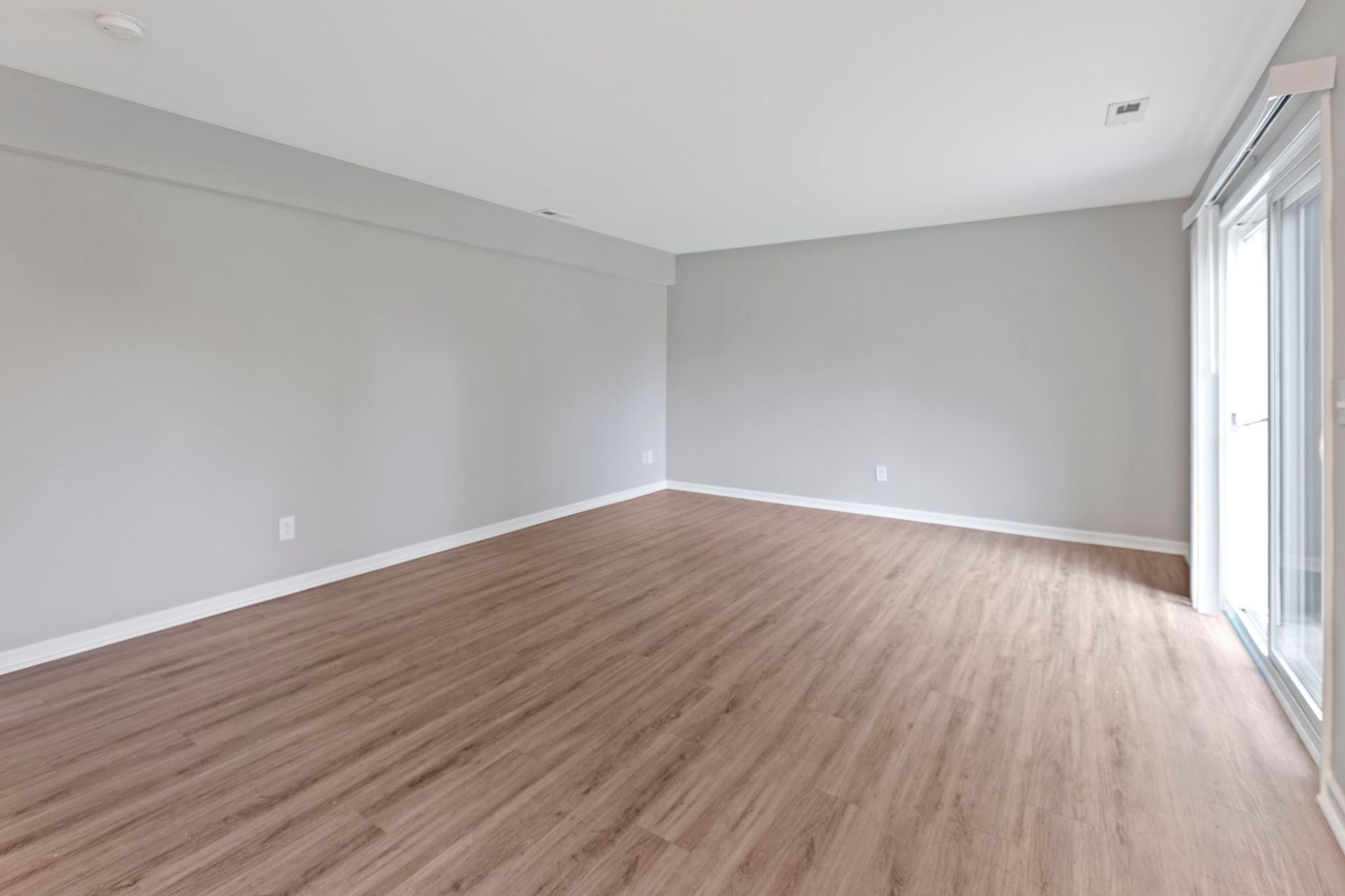 Empty room with gray walls, wood-look flooring, and a sliding glass door.