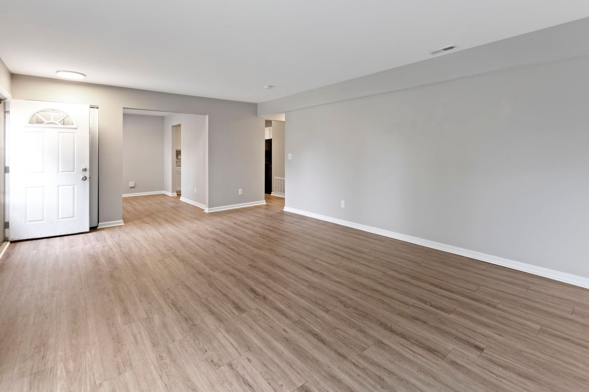 Empty living room with gray walls, wood-look flooring, and white front door.