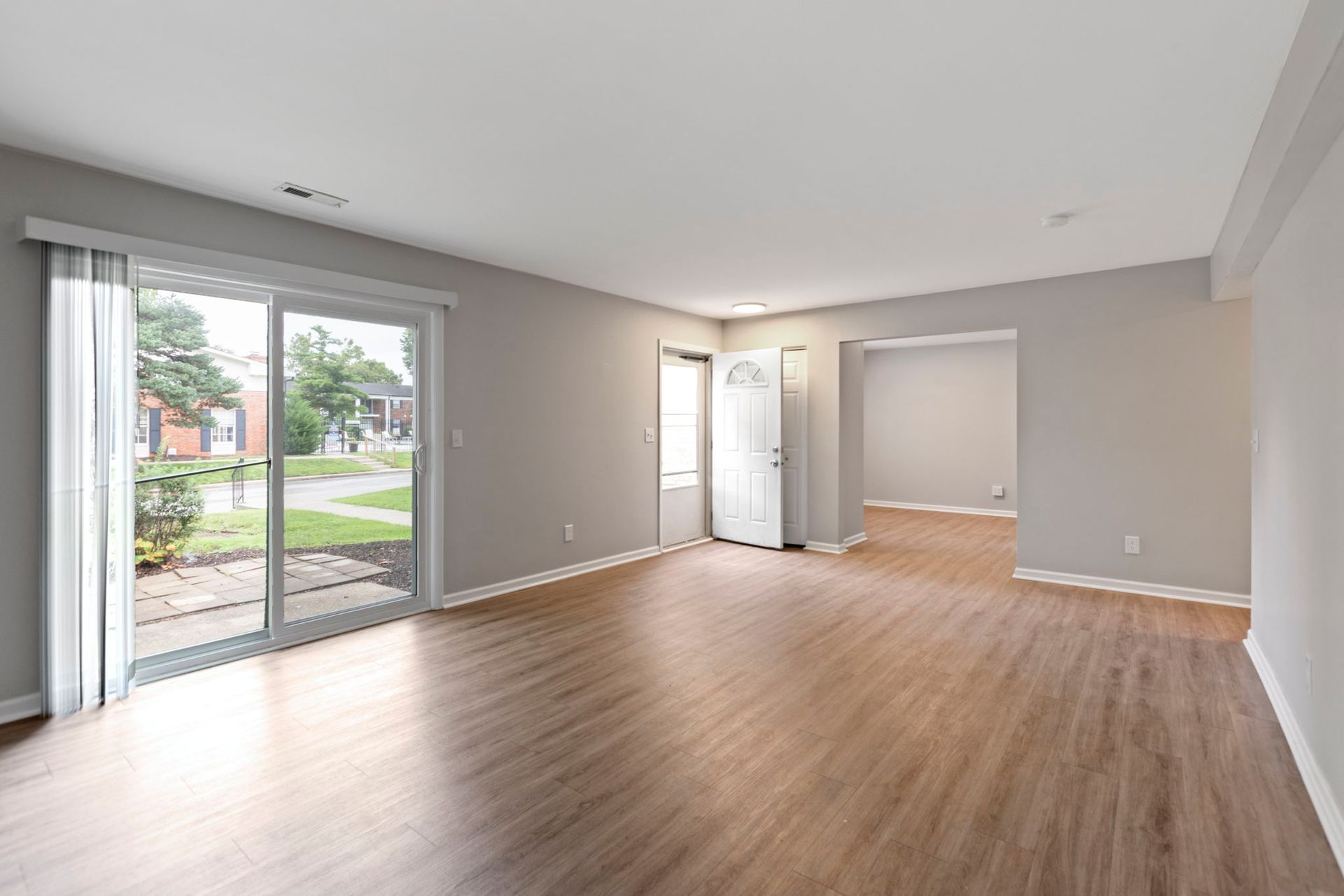 Empty living room with sliding glass door and wood-look floors. Gray walls, white door and trim.