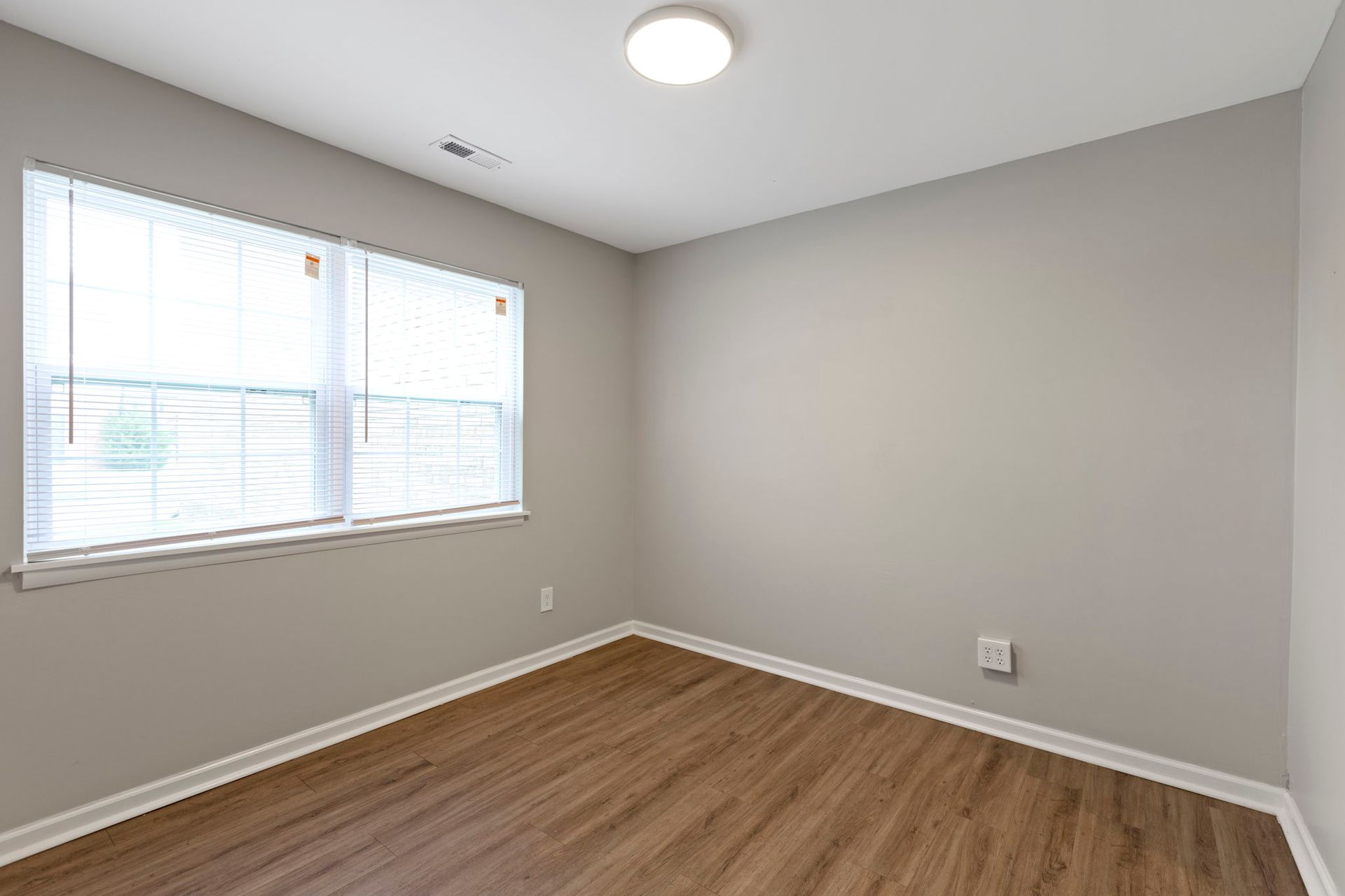 Empty room with wood-look floor, window with blinds, and light gray walls.