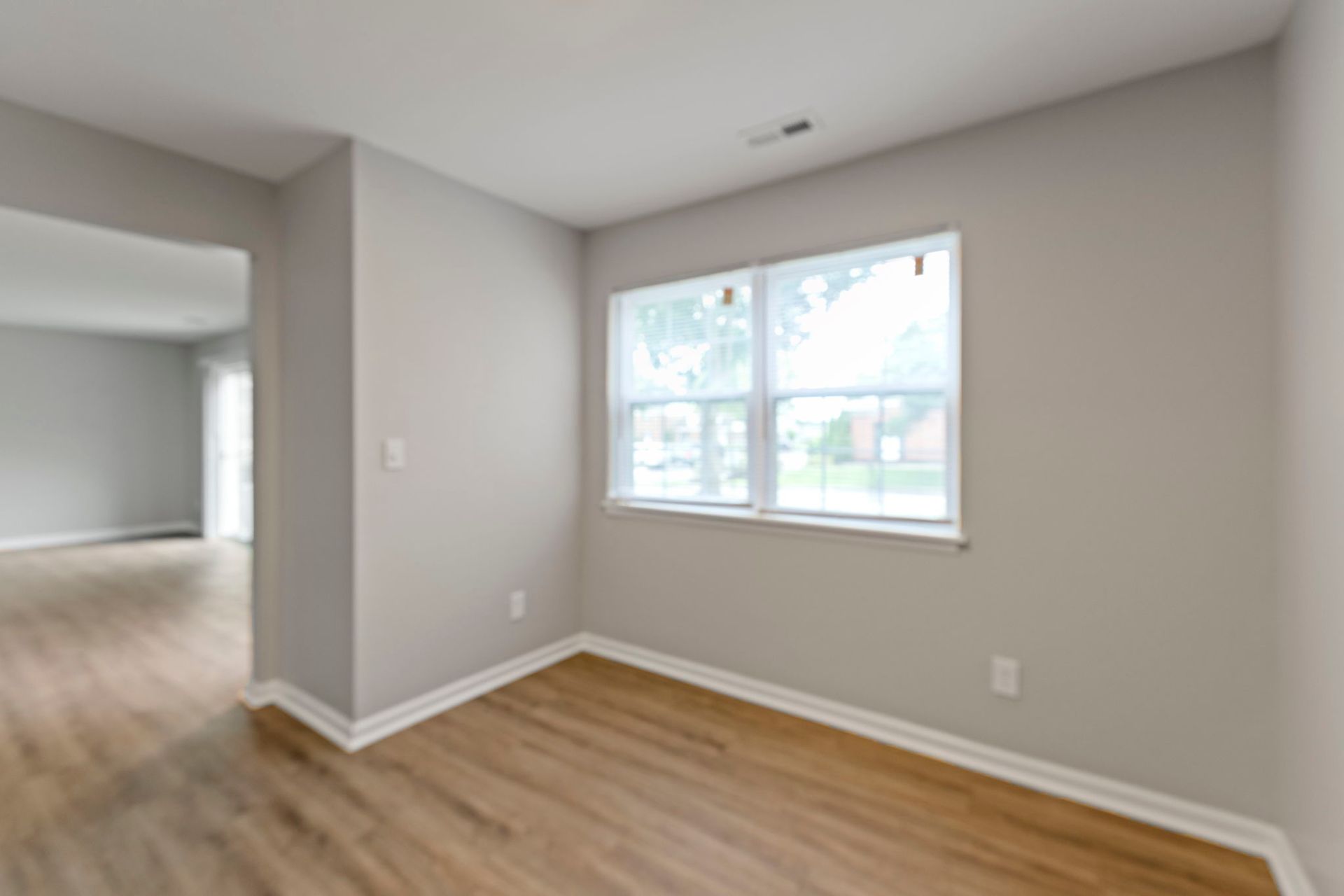 Empty room with light wood floors, gray walls, and a window.