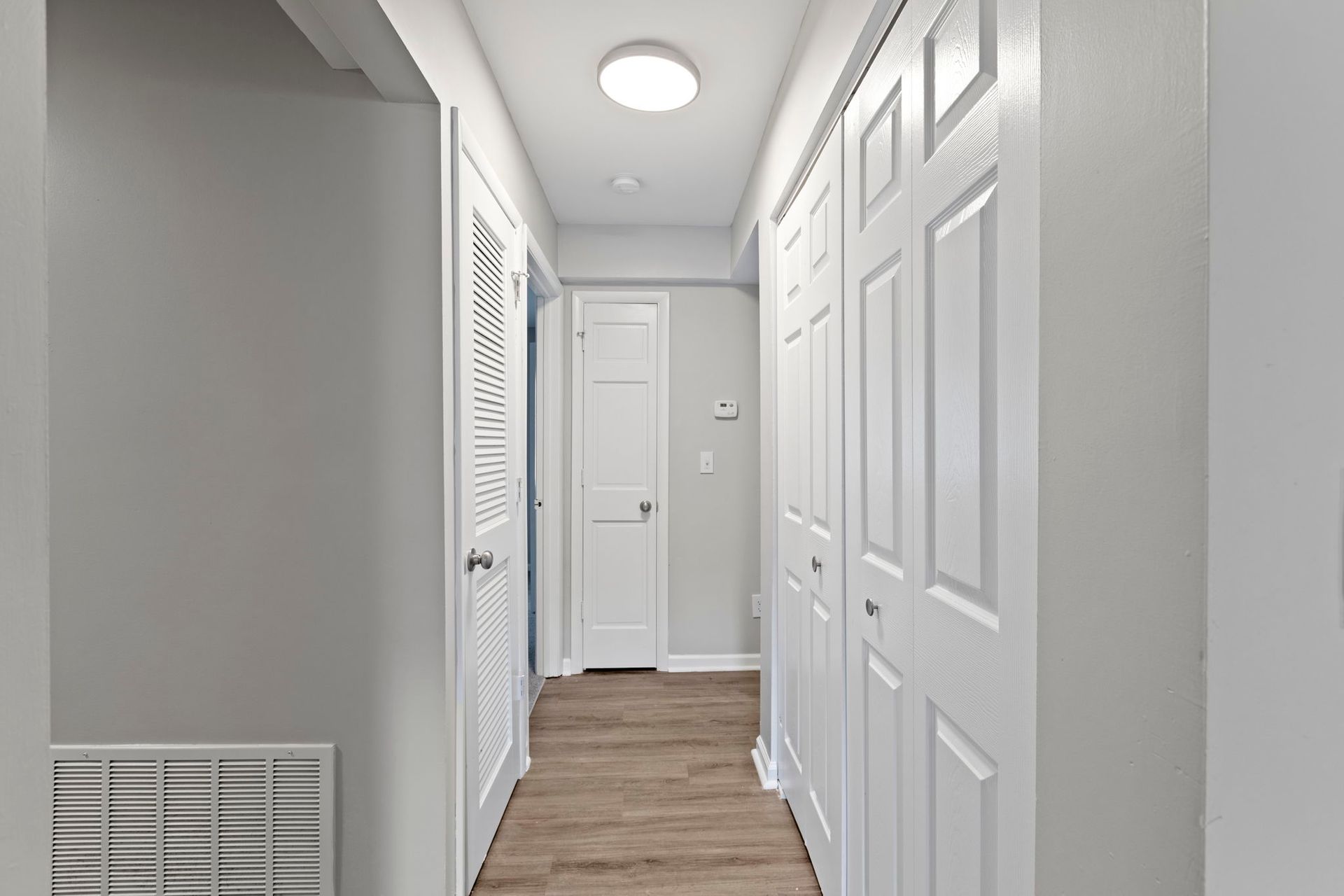 Narrow hallway with white doors, gray walls, and light-colored wood-look flooring.