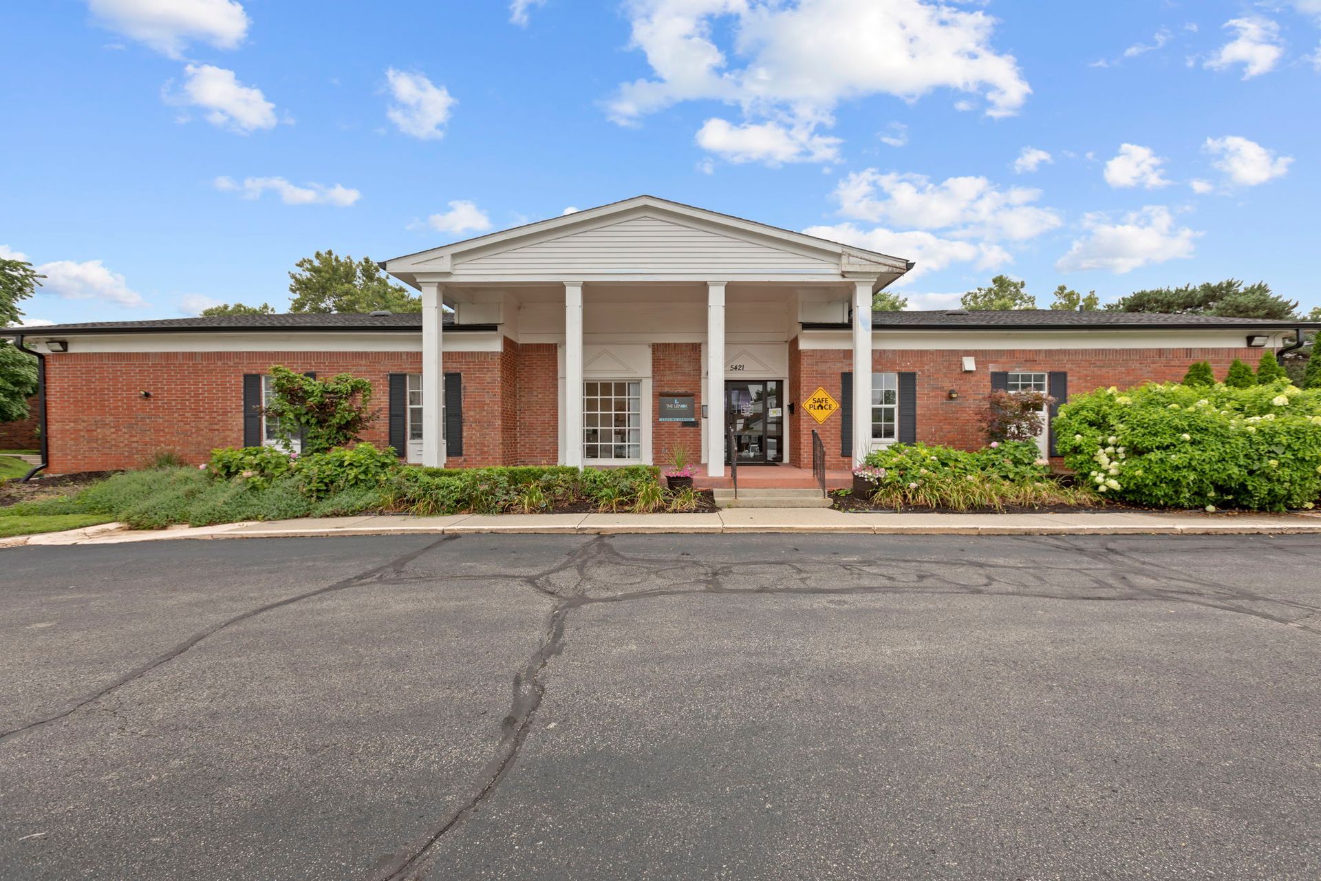 Red brick building with white columns and a cracked asphalt driveway under a blue sky.