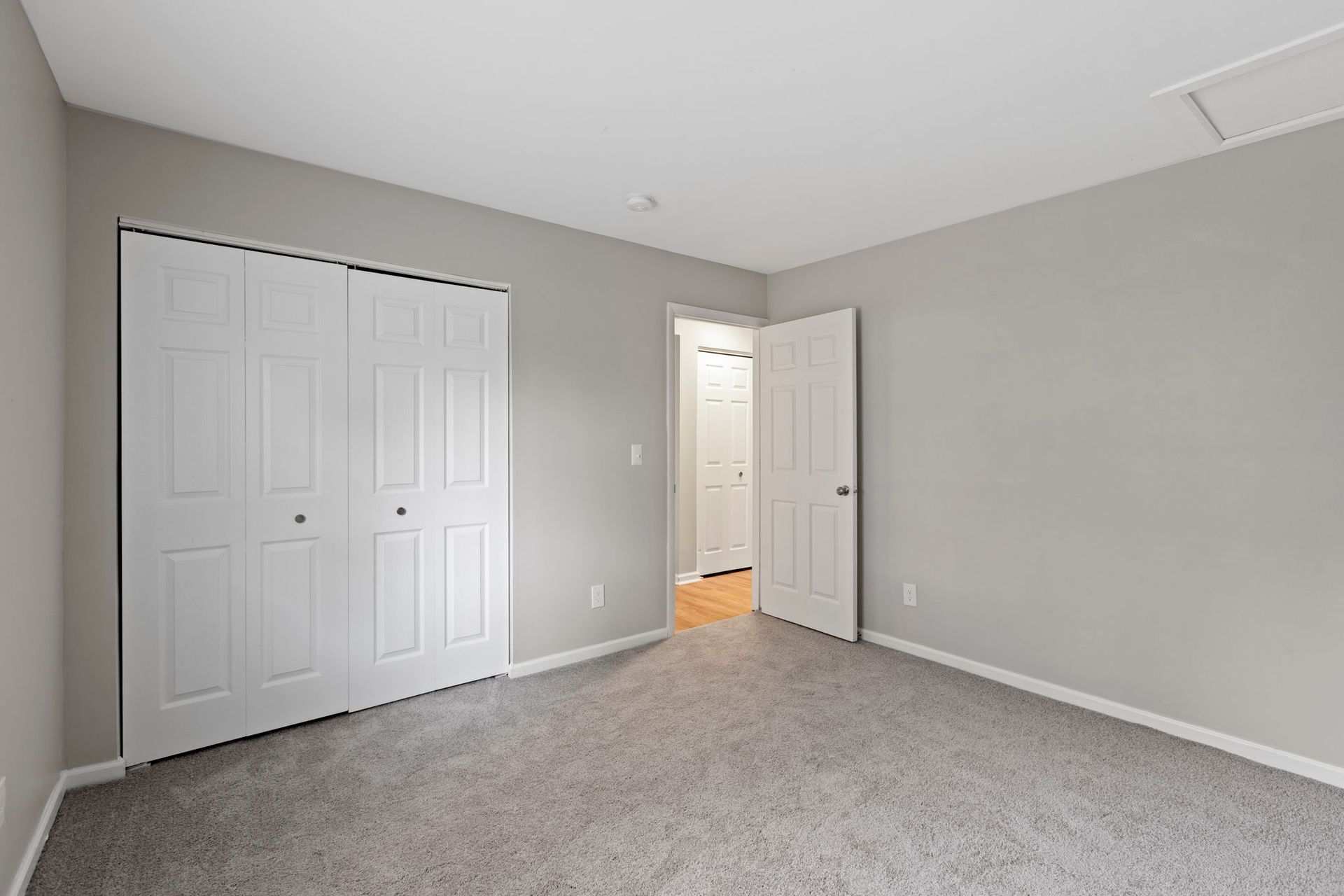 Empty bedroom with grey walls, carpet, white closet doors, and open doorway.