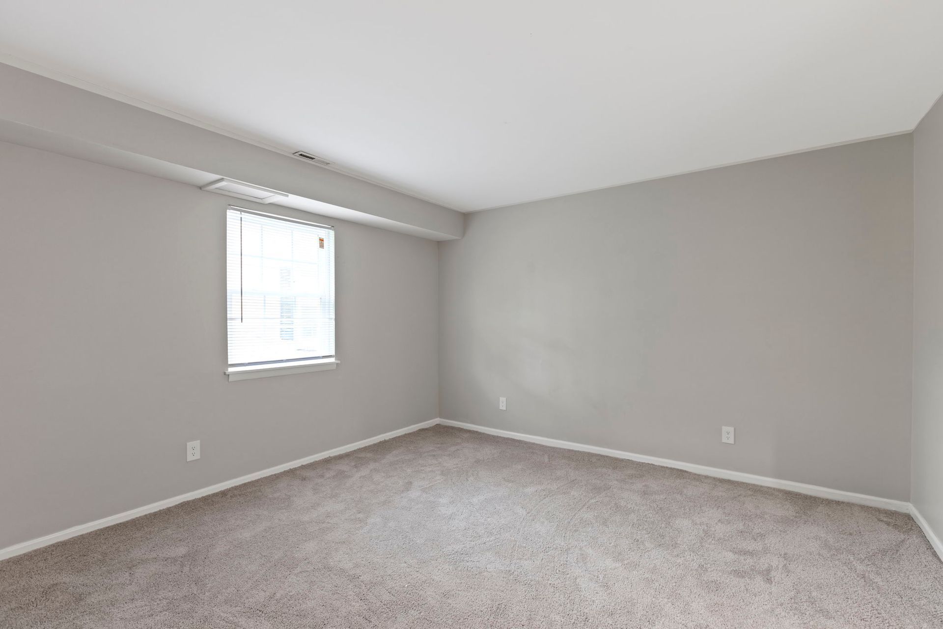 Empty room with gray walls, carpet, and a window with blinds.