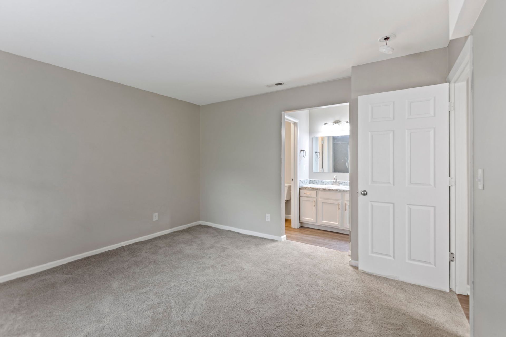 Empty bedroom with gray walls, carpet, and a doorway to a bathroom.