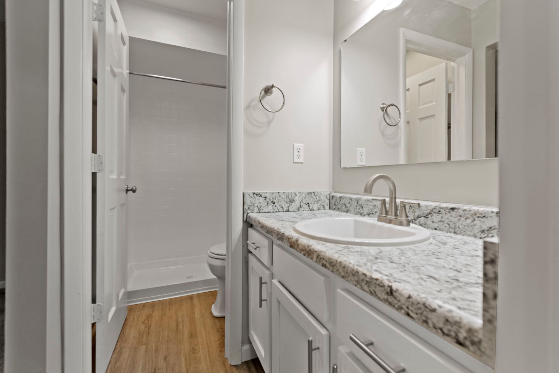 White bathroom with granite countertop, a shower, and a mirror.