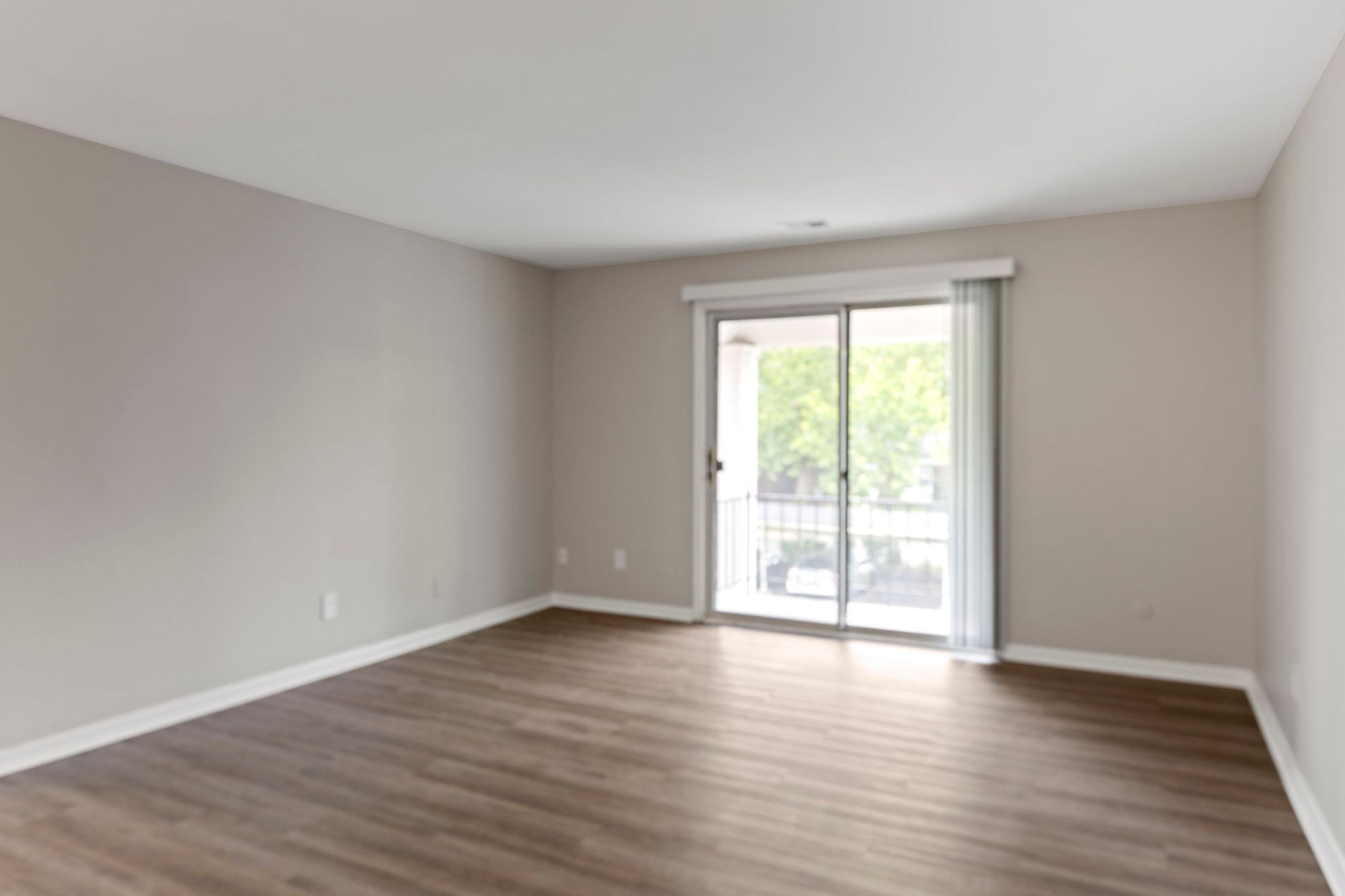 Empty room with hardwood floor, tan walls, and sliding glass door to a balcony.