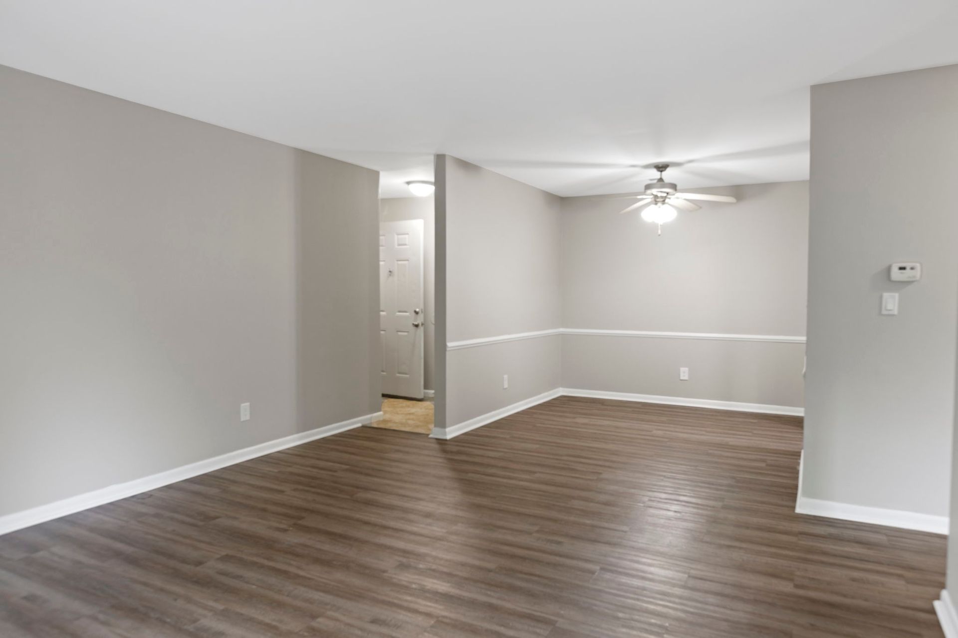 Empty living room with gray walls, dark wood floor, white trim, and ceiling fan.