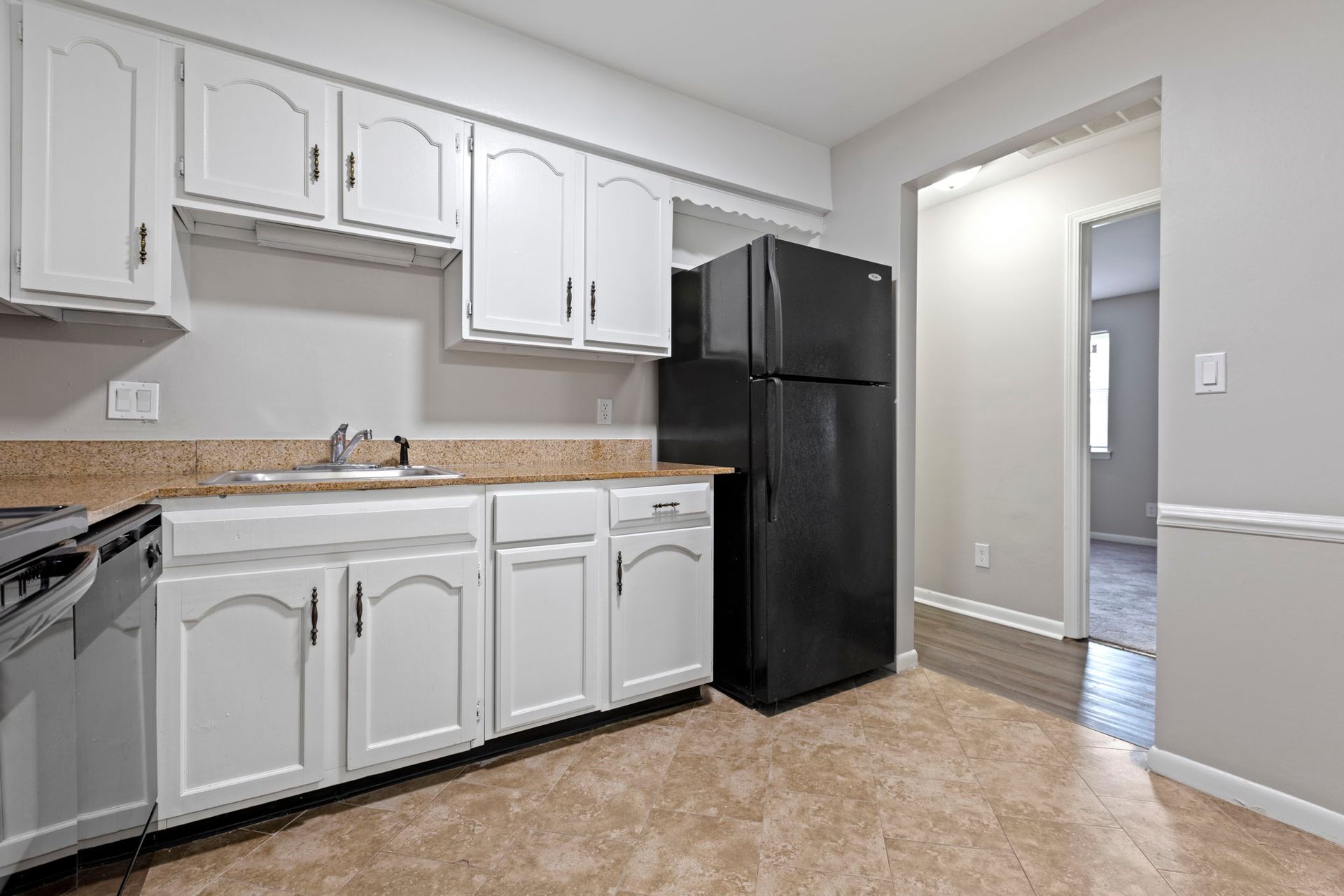 White kitchen with light countertops, black refrigerator, and a view into another room.