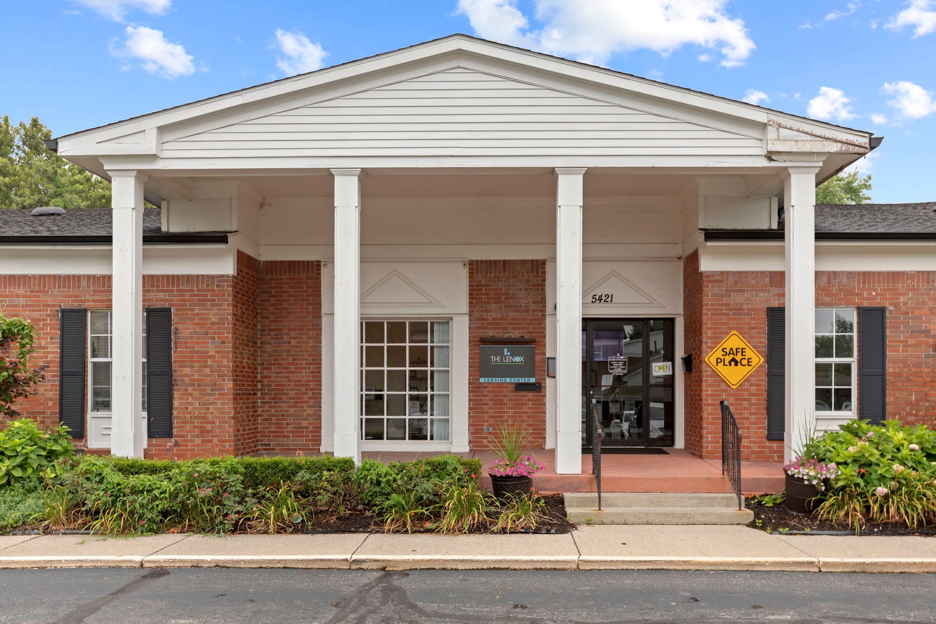 Red brick building with white columns and entrance; shrubs and dark shutters.