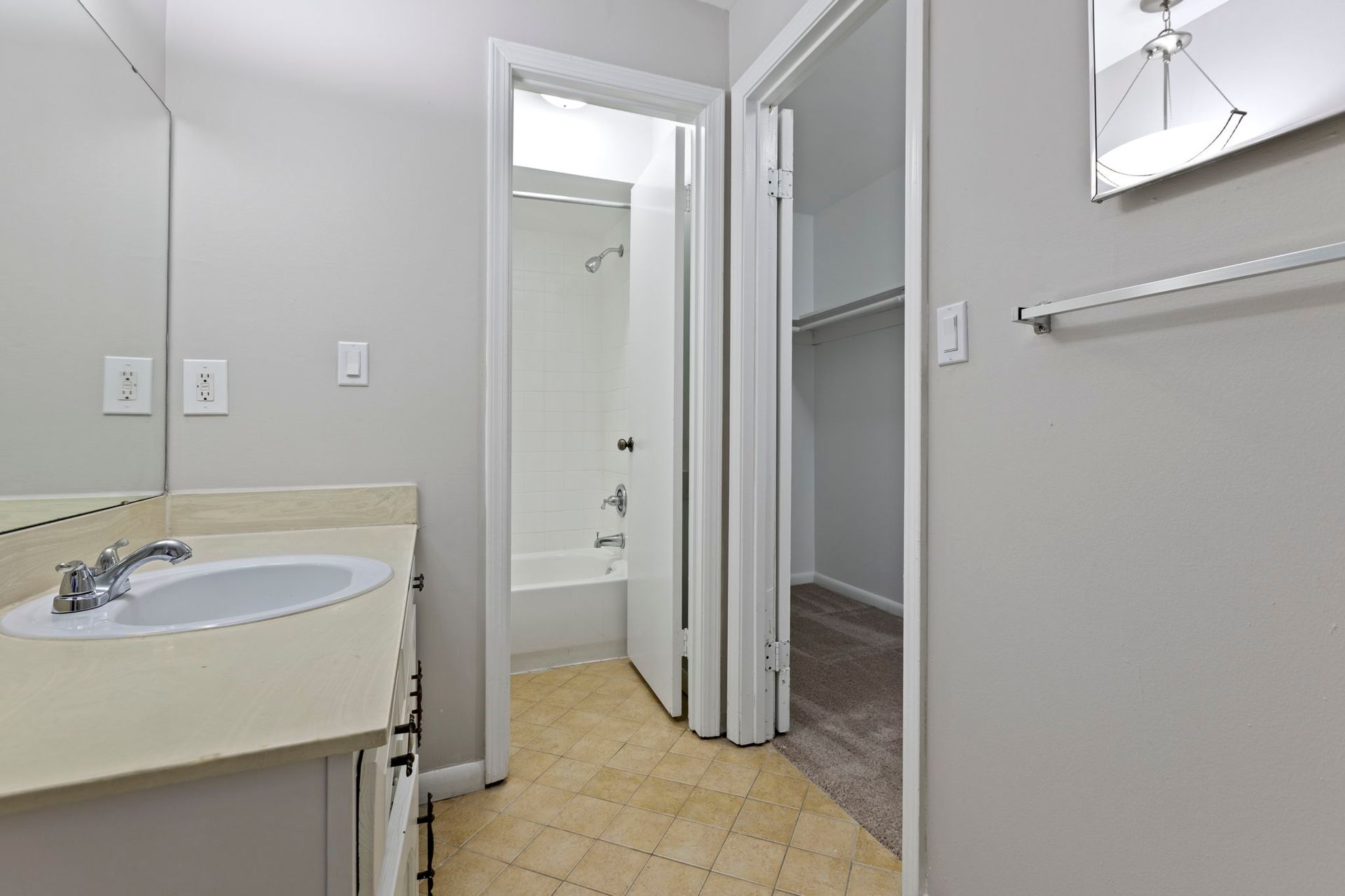 Bathroom with vanity, shower, and open closet; light gray walls, beige floors.