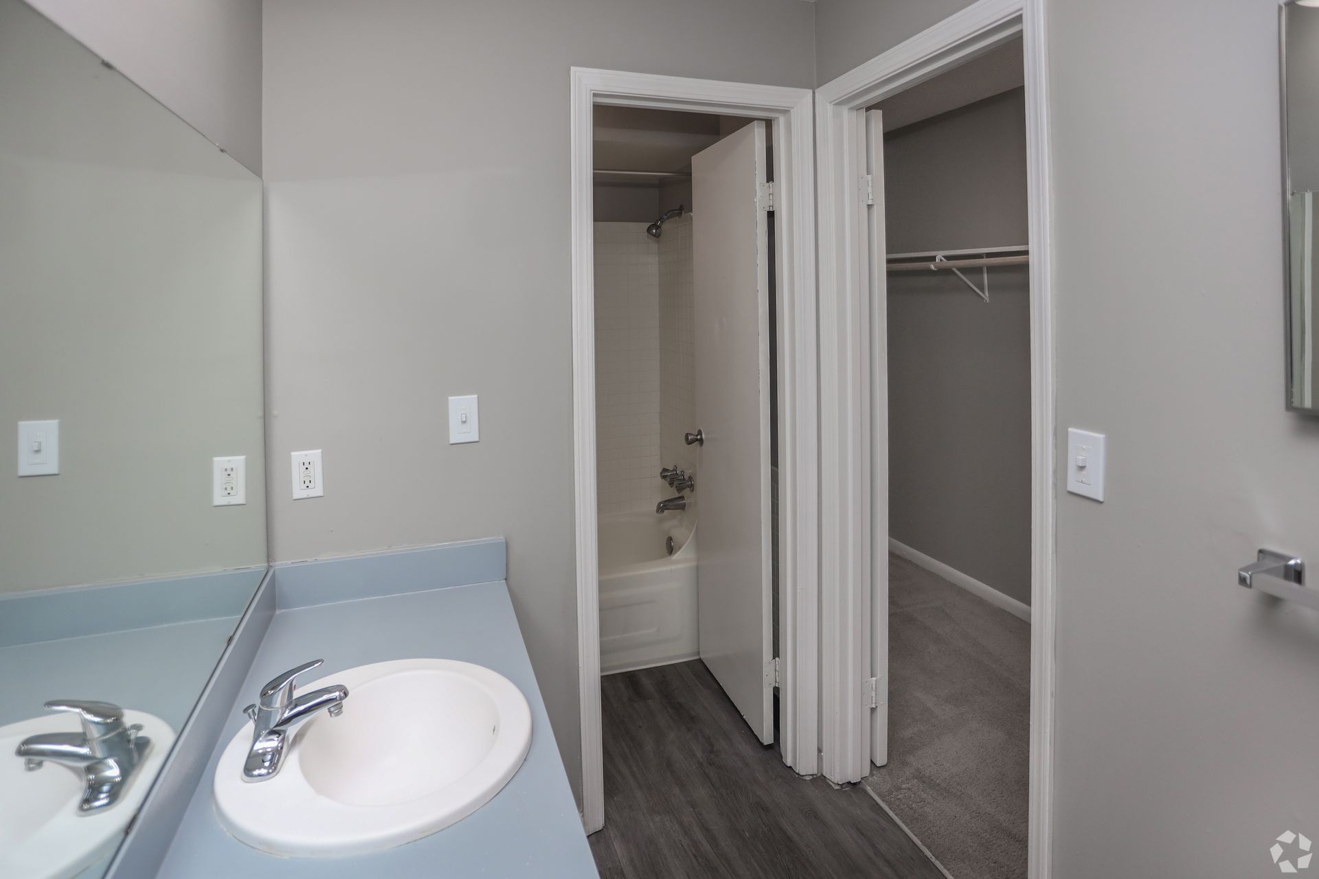Bathroom with a sink, mirror, shower, and closet. Gray walls and blue countertop.