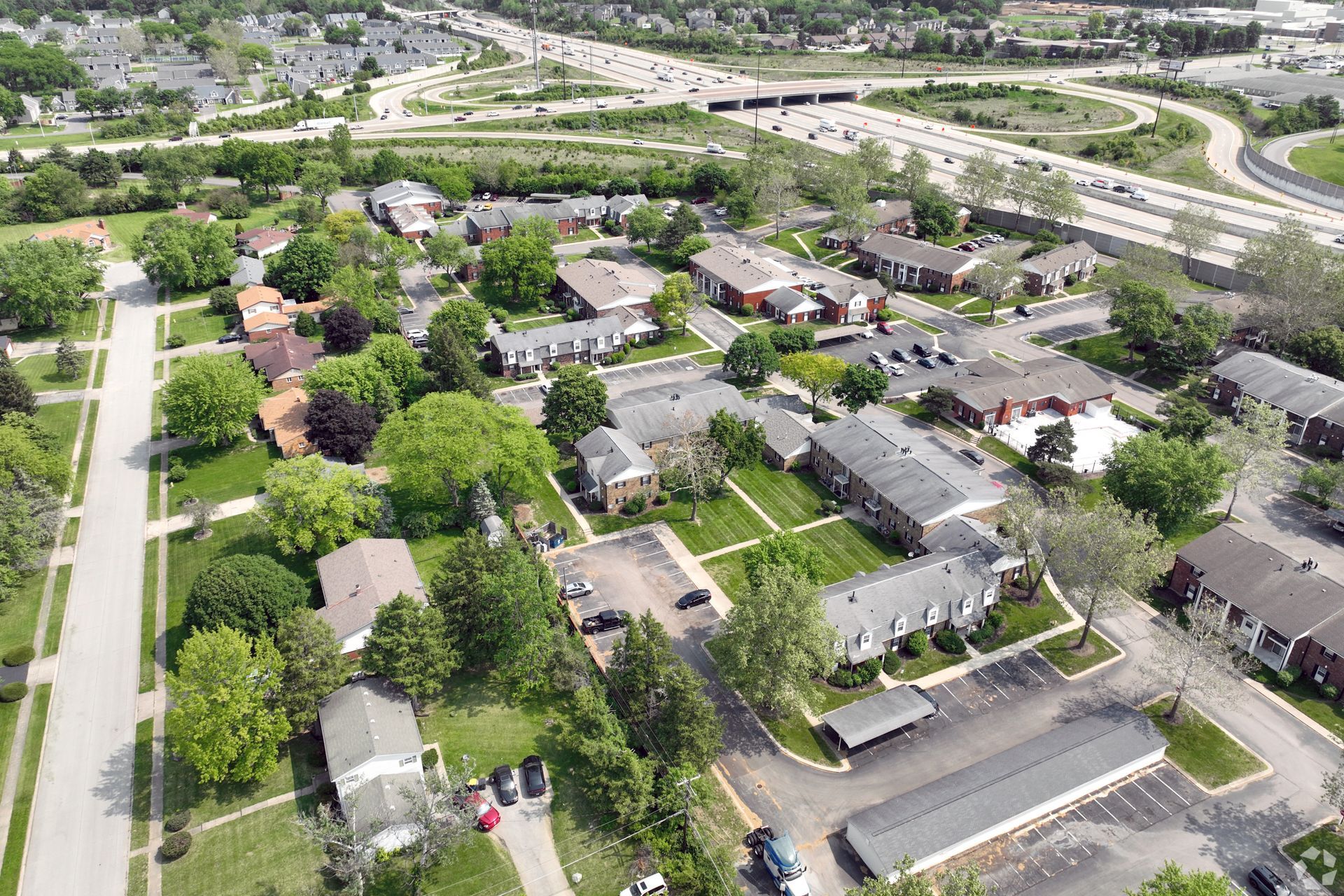 Aerial view of suburban homes and green trees near a highway interchange.