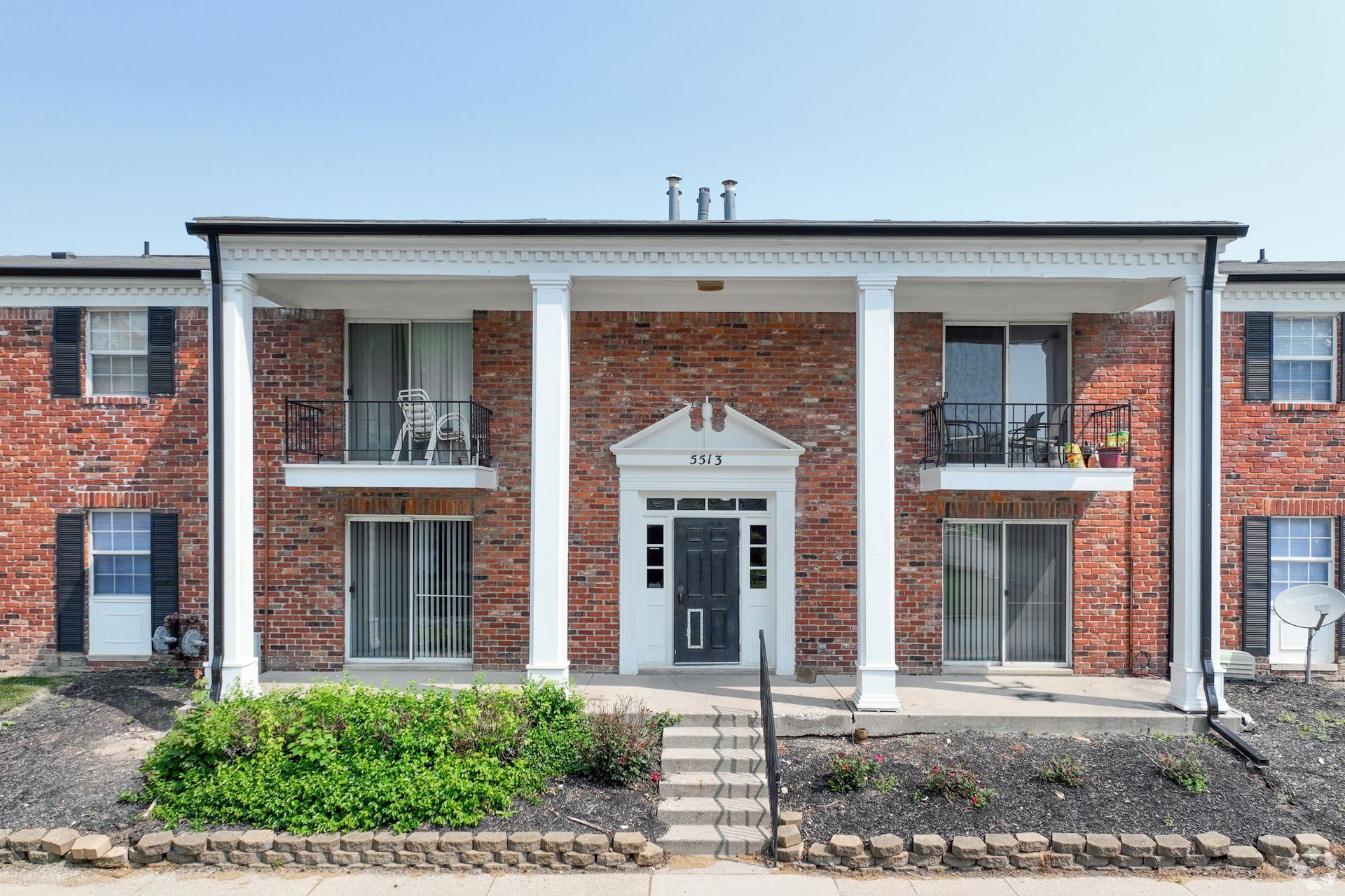Brick apartment building with white columns, balconies, and black shutters.