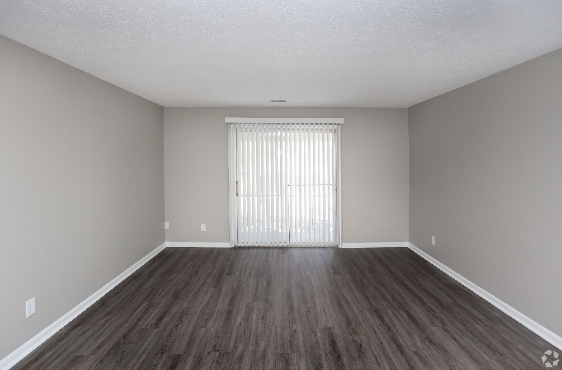 Empty room with gray walls, dark wood-look floor, and a sliding glass door with white vertical blinds.
