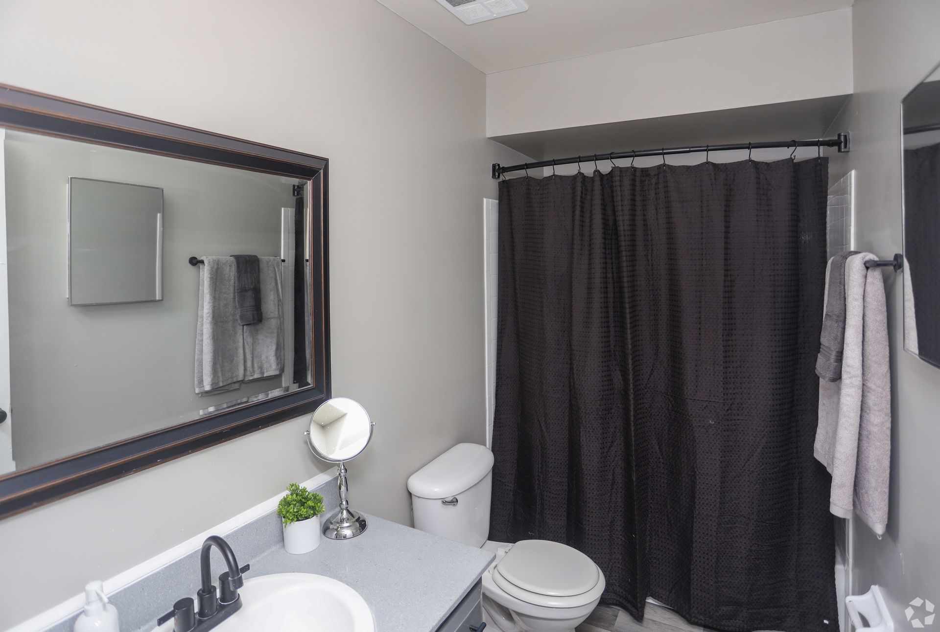 Bathroom with dark brown shower curtain, sink, toilet, mirror, and light gray walls.