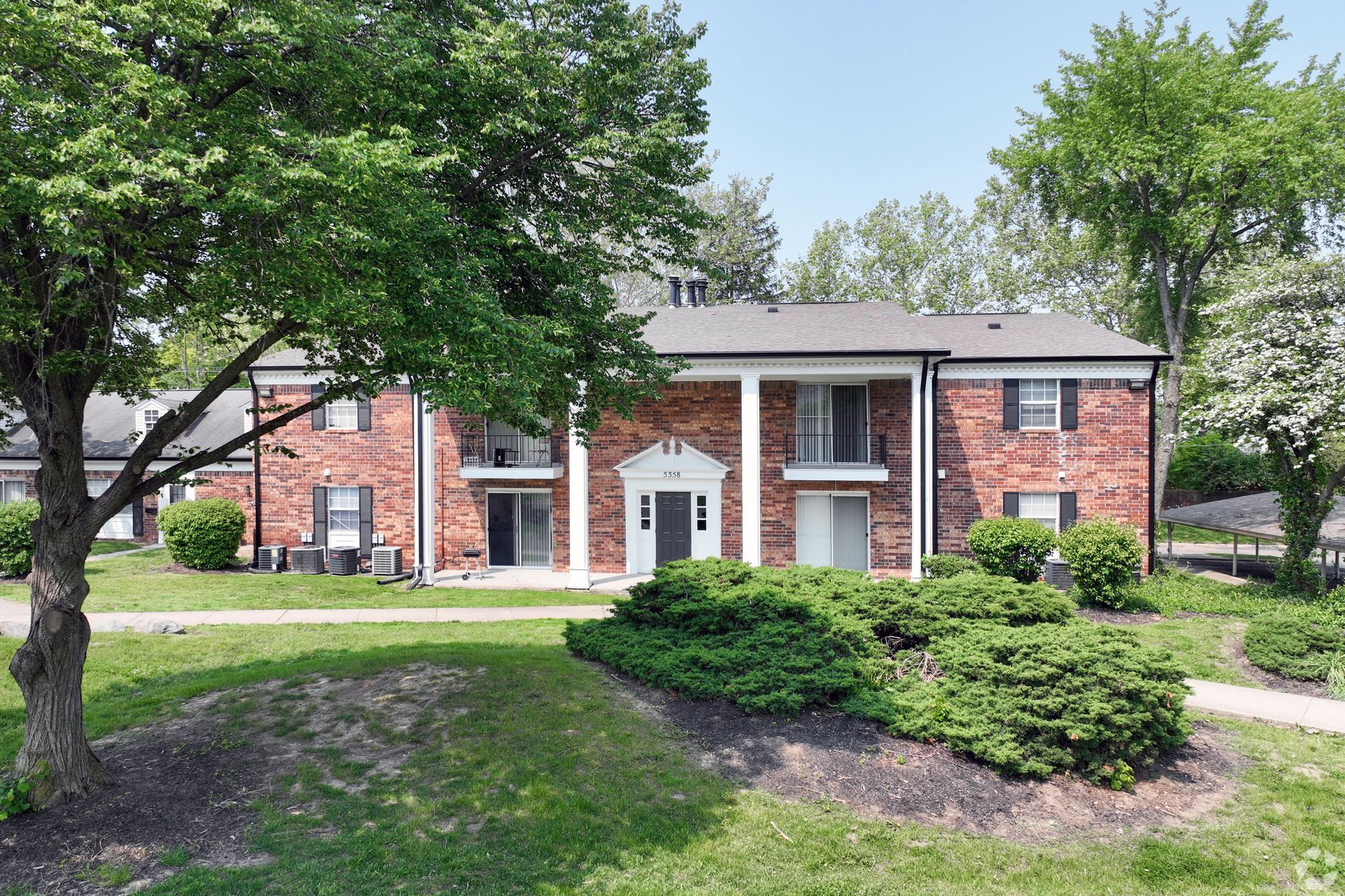 Red brick apartment building with white columns and green landscaping.