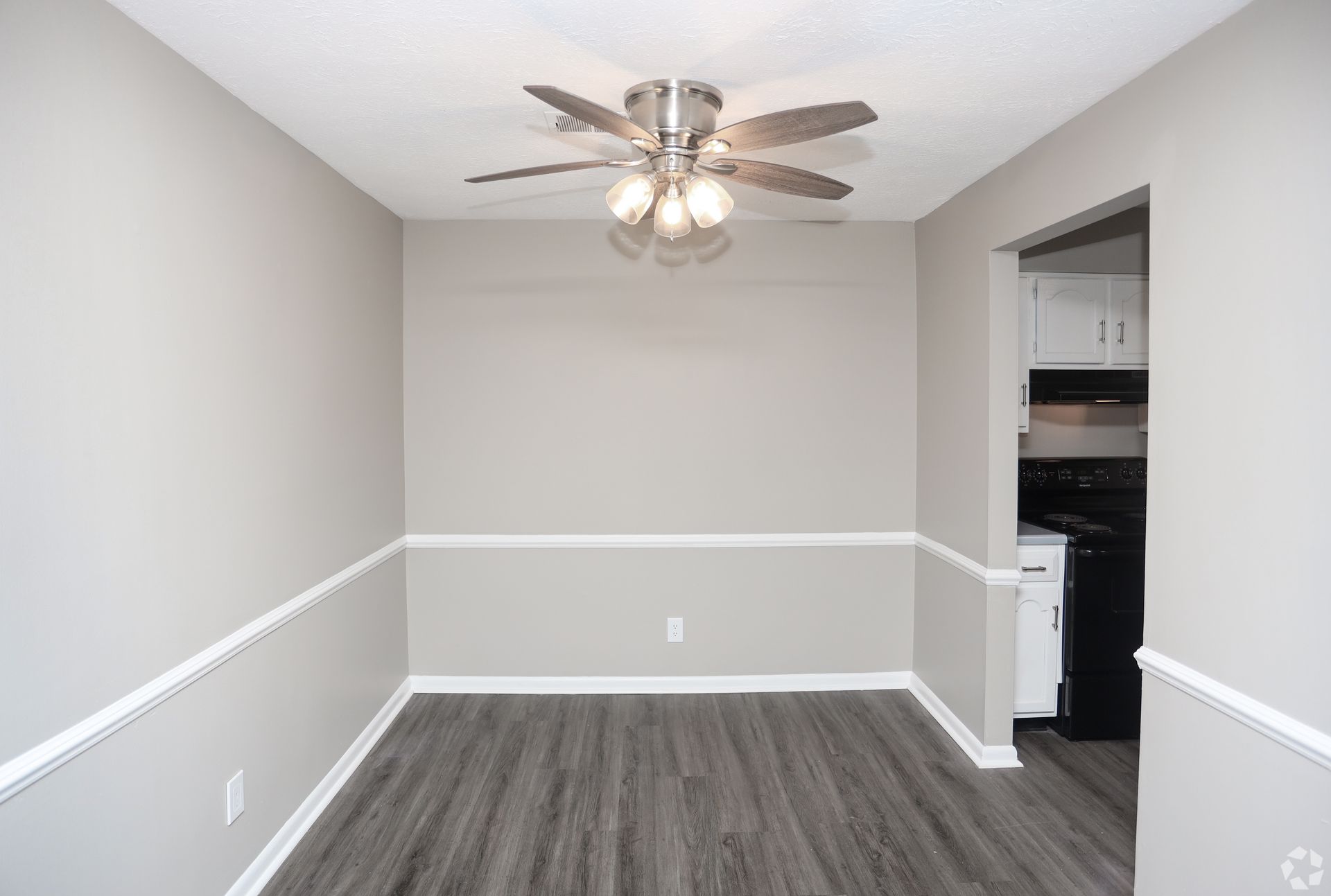 Empty dining room with gray walls, white trim, dark wood-look flooring, and a ceiling fan.