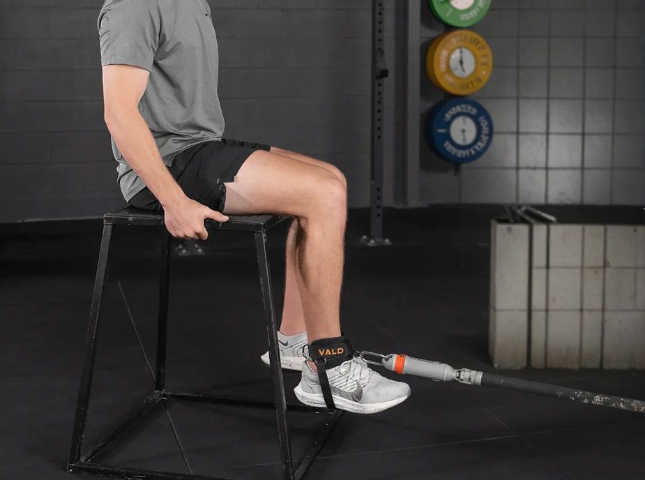 A man is sitting on a box with his legs crossed in a gym.