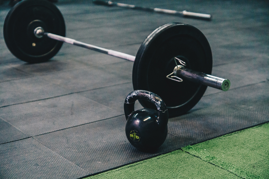 A barbell and a kettlebell are on the floor in a gym.