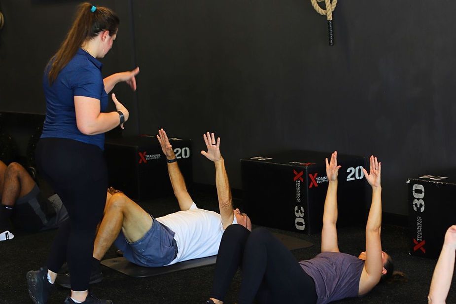 A woman is standing next to a group of people doing exercises in a gym.