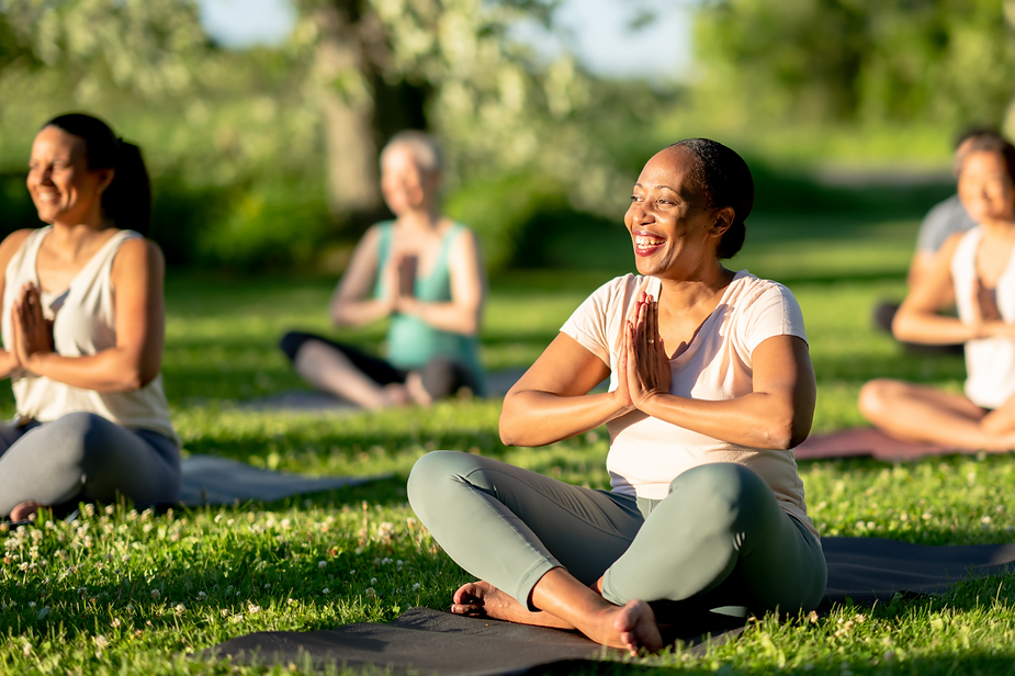 A group of women are sitting on yoga mats in a park.