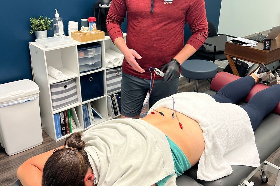 A man is standing next to a woman laying on a table.